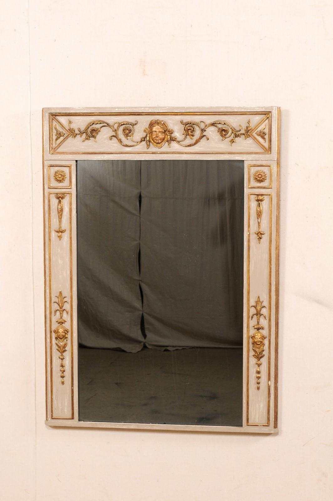 An Italian Neoclassical carved and gilt wood frame mirror from the 19th century. This antique mirror from Italy is rectangular in shape and features a putto carved prominently within its recessed top panel at center, flanked within scrolling foliate