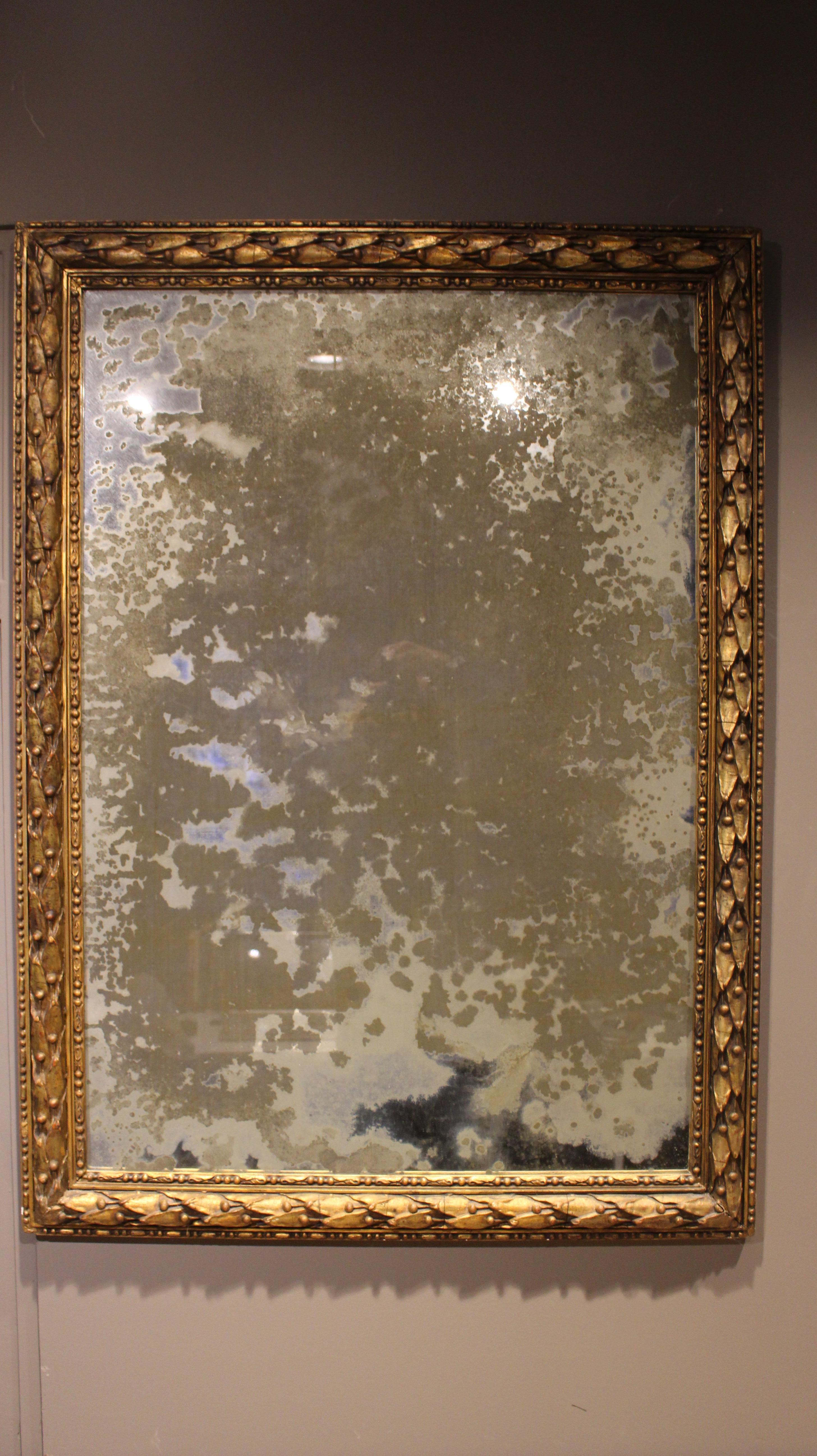 Un cadre italien néoclassique en bois doré et gesso avec un miroir ancien.  Le cadre, de style Louis XIII, est magnifiquement sculpté de motifs de coques et de baies et de détails de perles et d'enroulements sur le bord avant.