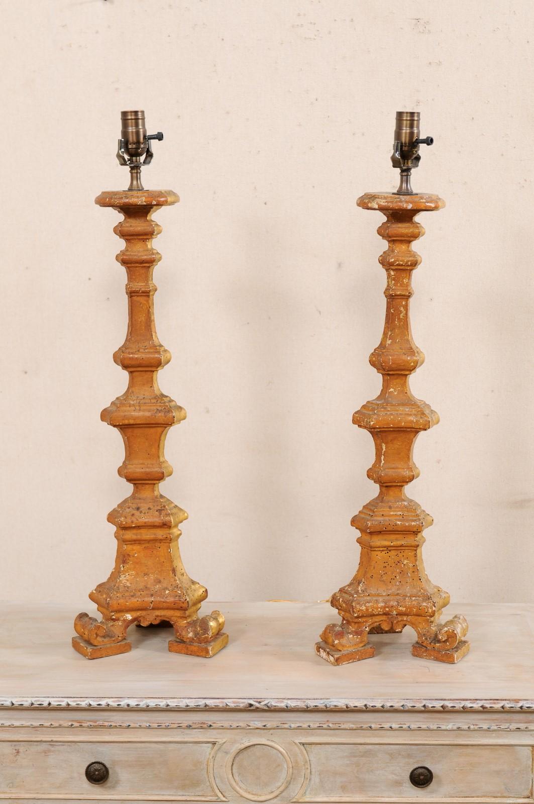 A pair of 19th century Italian candlestick lamps with their original gilt finish. This antique pair of table lamps from Italy each feature a 19th century hand-carved wooden candlesticks, with a circular neck (where the candlestick would have