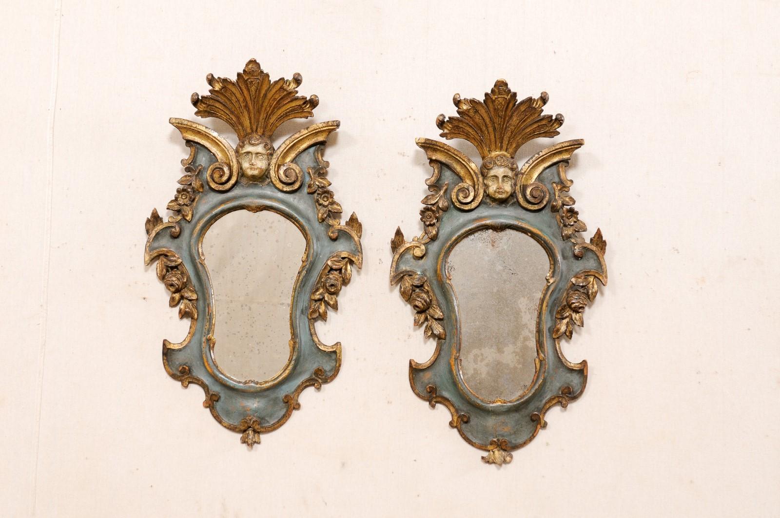 An Italian pair of small decorative Rococo style wall mirrors from the late 19th century. This pair of wall decorations from Italy have been created in Rococo style and carved with a leaf pediment top over a putto head at center, flanked within