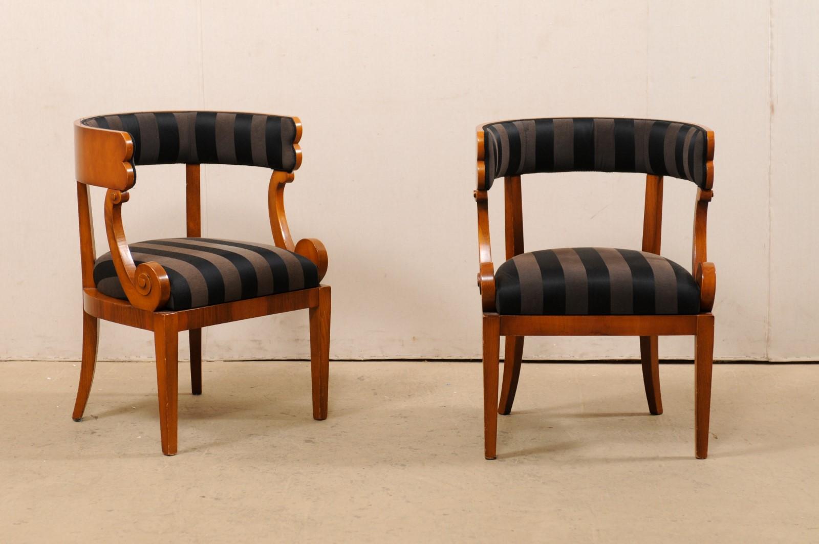 An Italian pair of barrel back occasional chairs. This vintage pair of chairs from Italy each feature barreled backrest supports, with arm supports at either side being carved in a lovely volute shape. Skirting is clean and simple, with chairs being