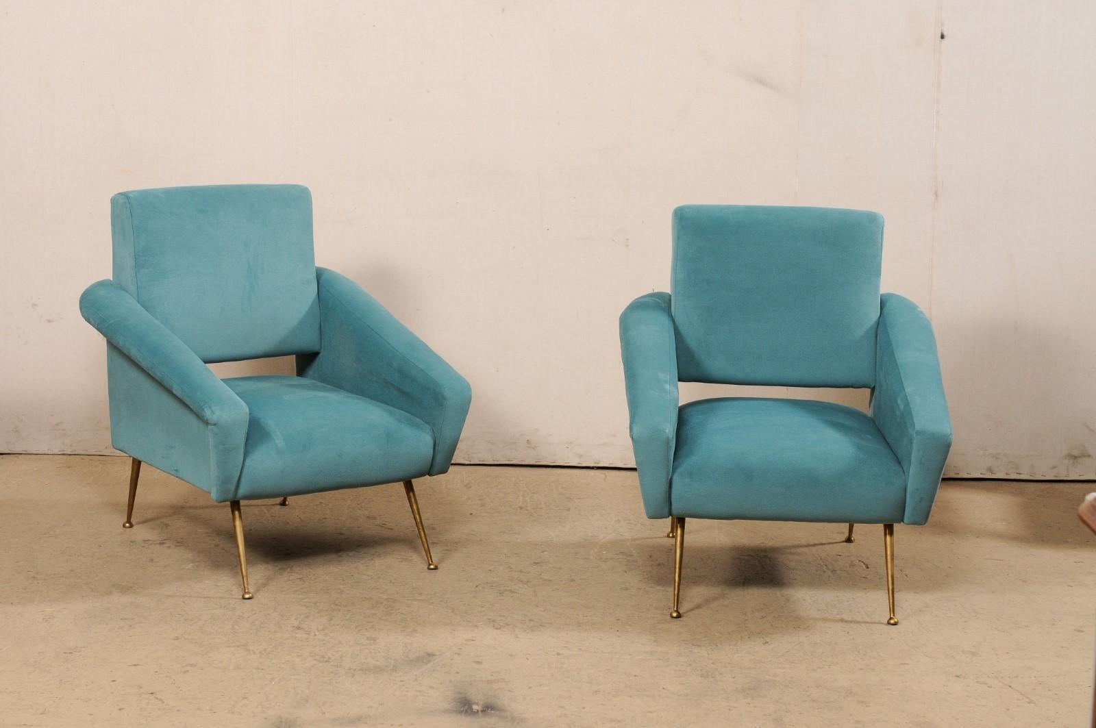 An Italian pair of chairs upholstered club chairs from the Mid-20th Century. These vintage arm chairs from Italy have a comfortably modern design with squared seats and backs, and full arms that angle downwards from the back sides towards their