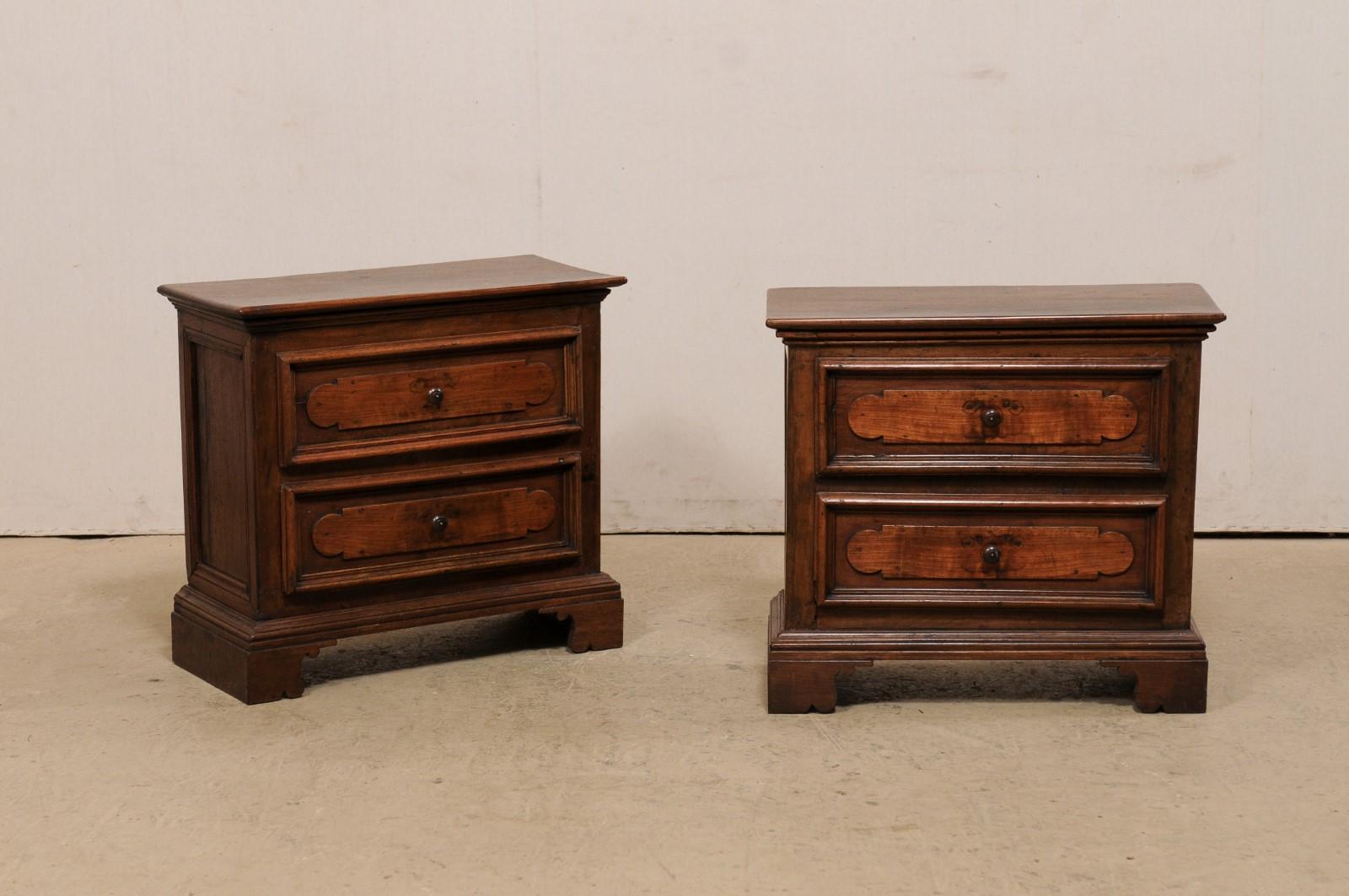 An Italian pair of walnut wood side chests from the mid 20th century. This pair of vintage commodes from Italy (mid-century in age, though were created from older wood) are each fitted with two drawers, and are raised upon a flat stacked molding