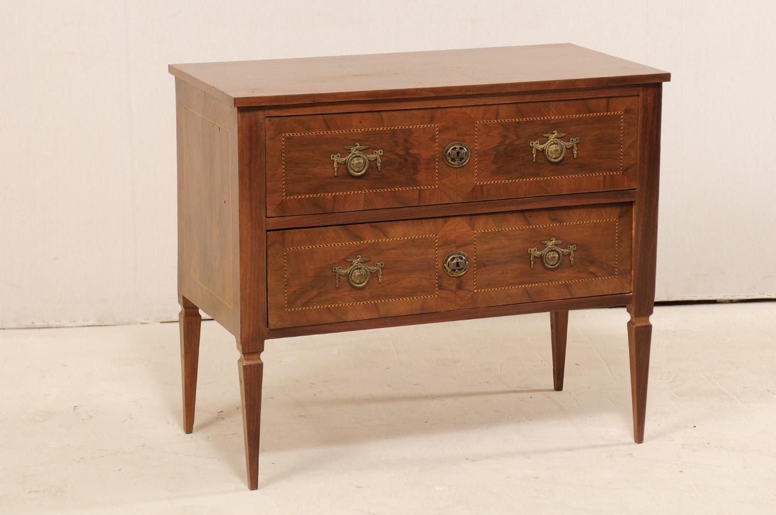 An Italian two-drawer chest from the early 20th century. This antique chest from Italy features delicate inlay banding about it's top, drawer fronts and each side. The cabinet houses two drawers, each fitted with a pair of decorative ring pulls