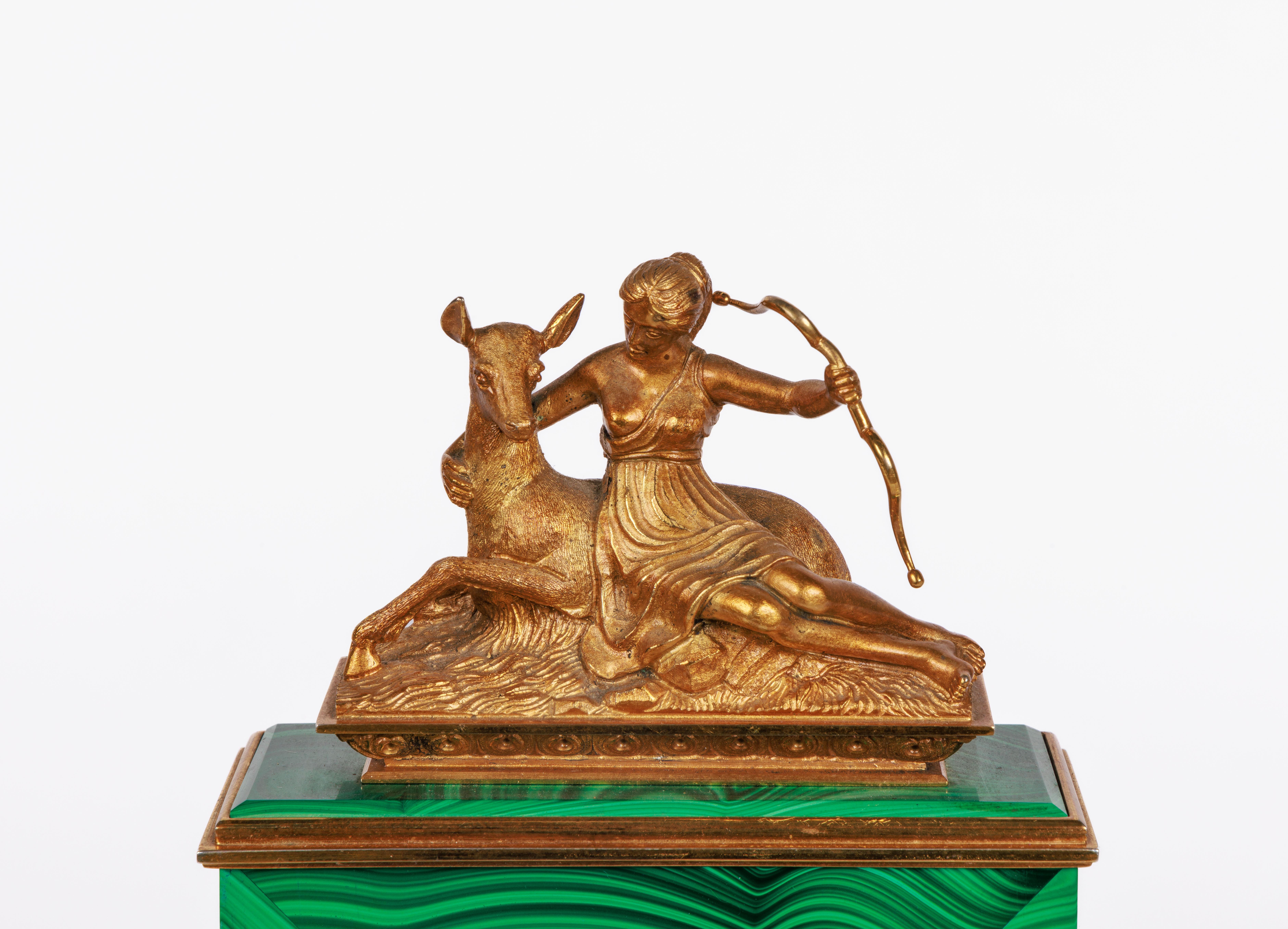 An Italian silver-gilt and figural malachite desk clock, circa 1960.

Beautiful malachite case with 22k gold plated on .800 silver mounts, trim and figure of Diana the huntress holding a bow and seated nestled to a deer which is laying down.