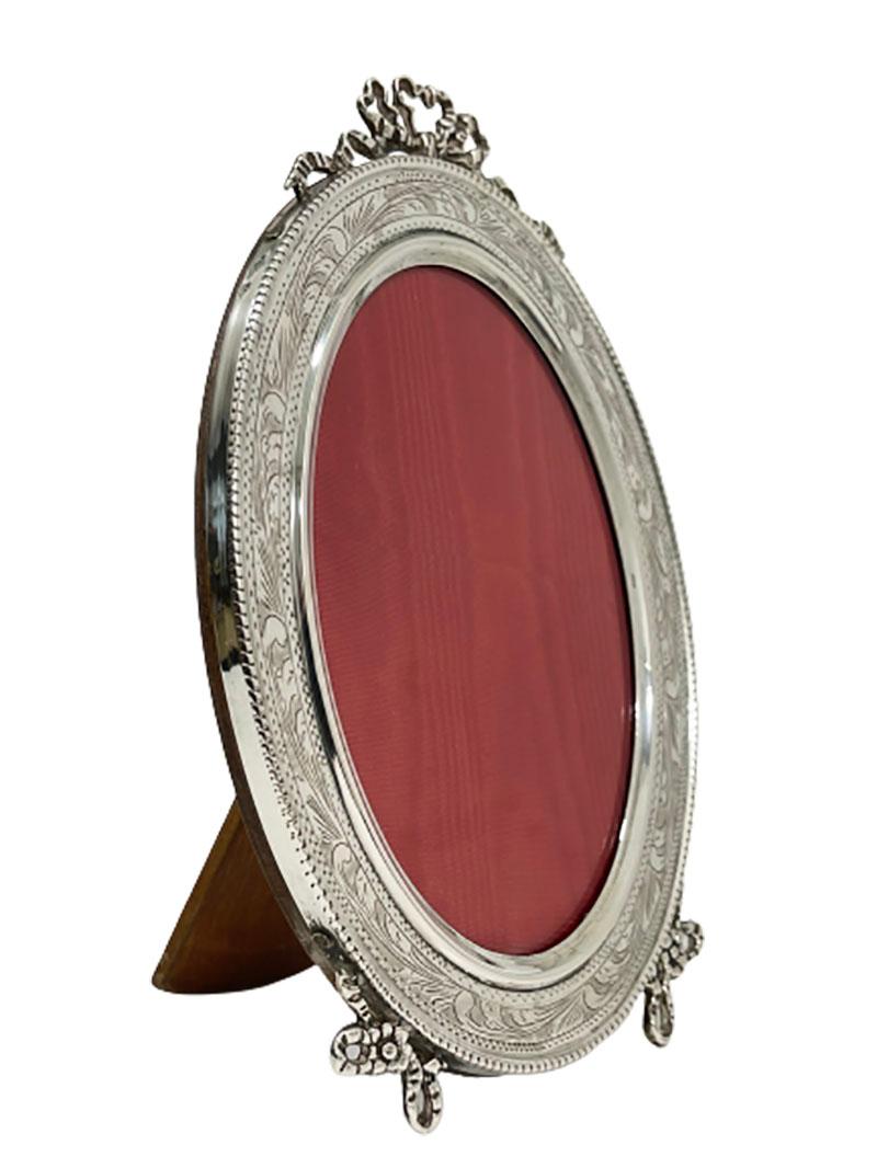 An Italian silver picture frame 

An oval silver picture frame, engraved and bow at the top and feet. 
A standing model on wooden stand and back.
Silver content is 800/ 1000

The frame measures: 
19 cm high, 13 cm wide and the depth standing