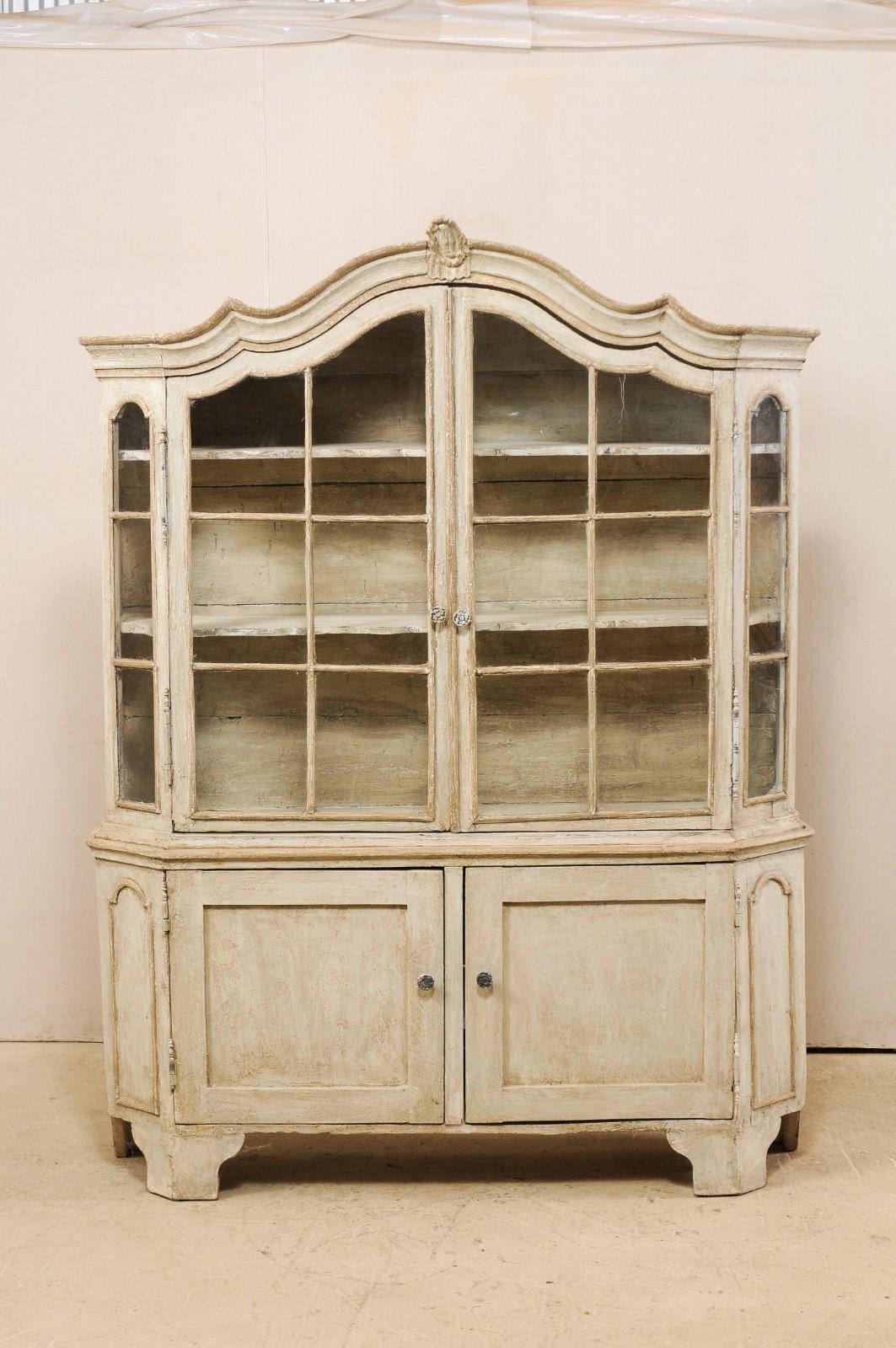 An Italian glass and painted wood display cabinet from the early 19th century. This tall cabinet from Italy has been fitted with a pair of upper glass doors and a pair of lower single panel enclosed doors directly below, and is raised upon bracket