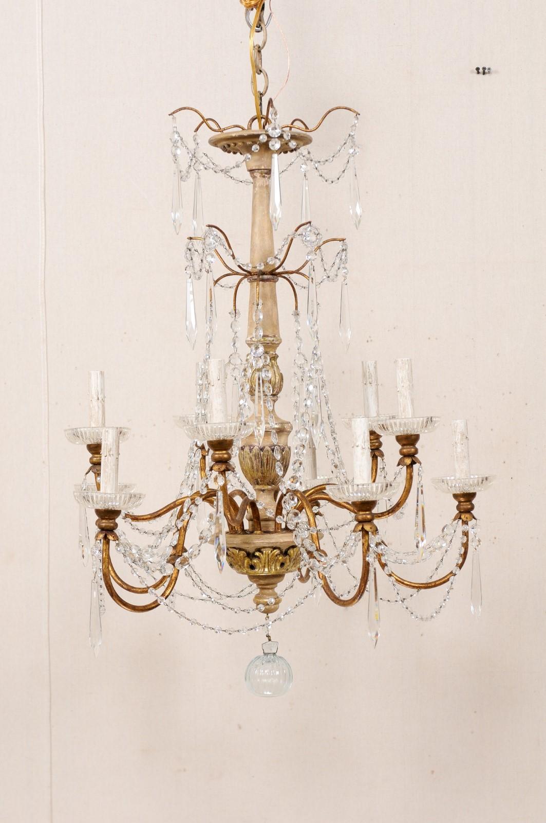 An Italian ten-light wood column style chandelier with crystal adornment from the mid-20th century. A chandelier from Italy features a decoratively carved central wood column with gilt acanthus leaf motif, and a prominent two-tiered splayed crystal