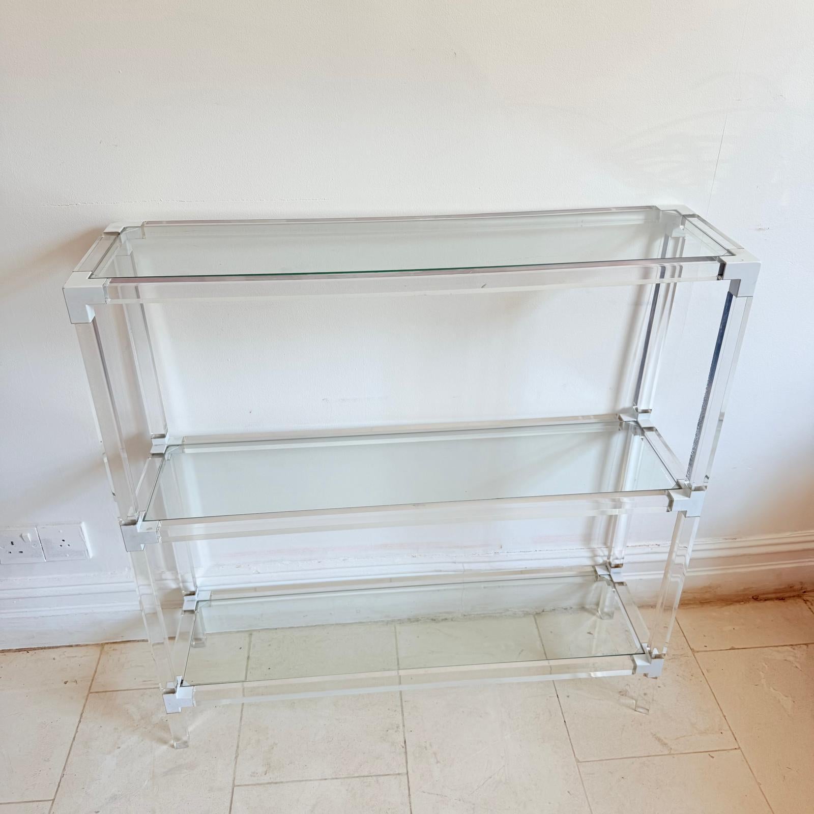 Italian c.1960's design seamlessly fuses glamor, and modernist appeal. Crafted in thick Lucite with painted white metal accents, the three-tier console table features inset glass shelves