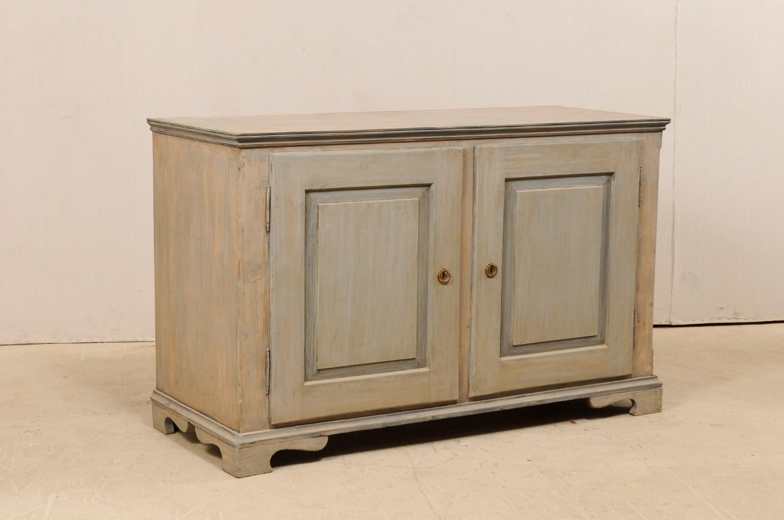 An Italian painted wood two-door cabinet from the 19th century. This antique Italian cabinet features two raised panel doors housed within a plainly decorated case, flanked by straight line molding beneath top edge and skirt. The buffet is raised on