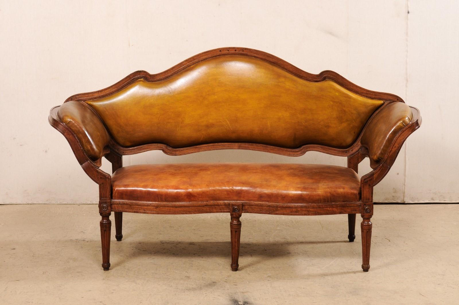 An Italian Venetian leather upholstered sofa from the 19th century. This antique settee from Italy features a elegantly dramatic arched top rail at backside that descends into padded, out-swept arms. The walnut frame surrounds the leather
