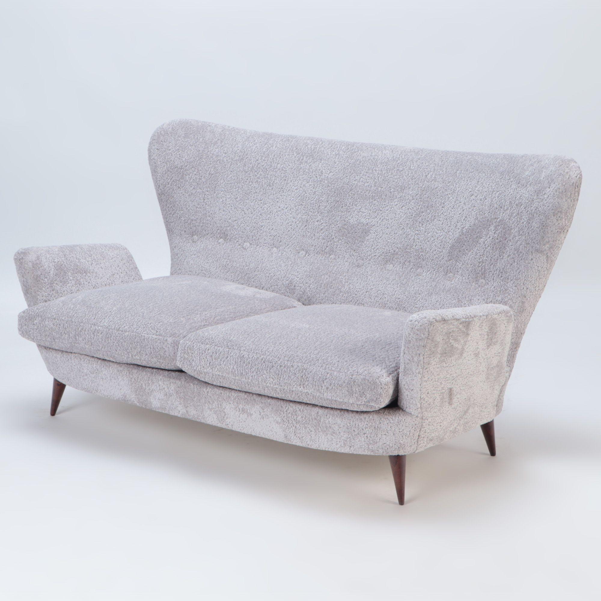 A stylish Italian vintage wingback drop arm upholstered settee, resting on four angled wooden legs.