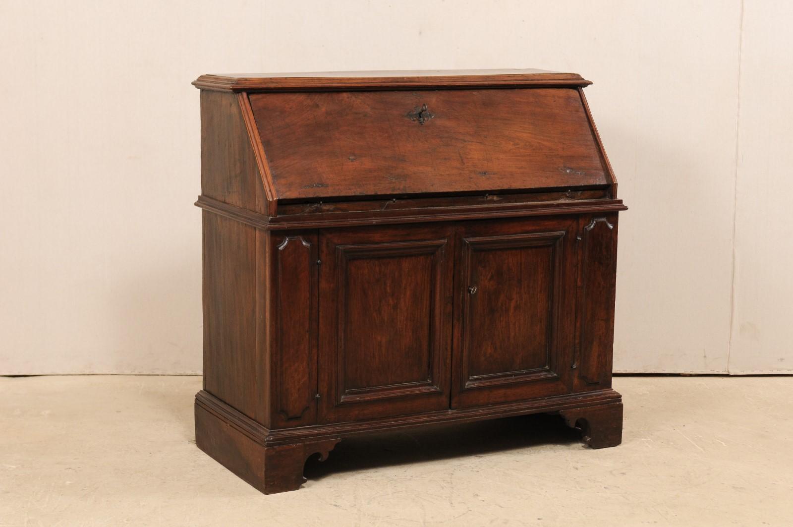 A handsome Italian drop-front secretary cabinet from the 18th century. This antique bureau of walnut wood from Italy features a slanted fall front door, which opens to reveal a nice writing surface and interior display of six compartments. Below the
