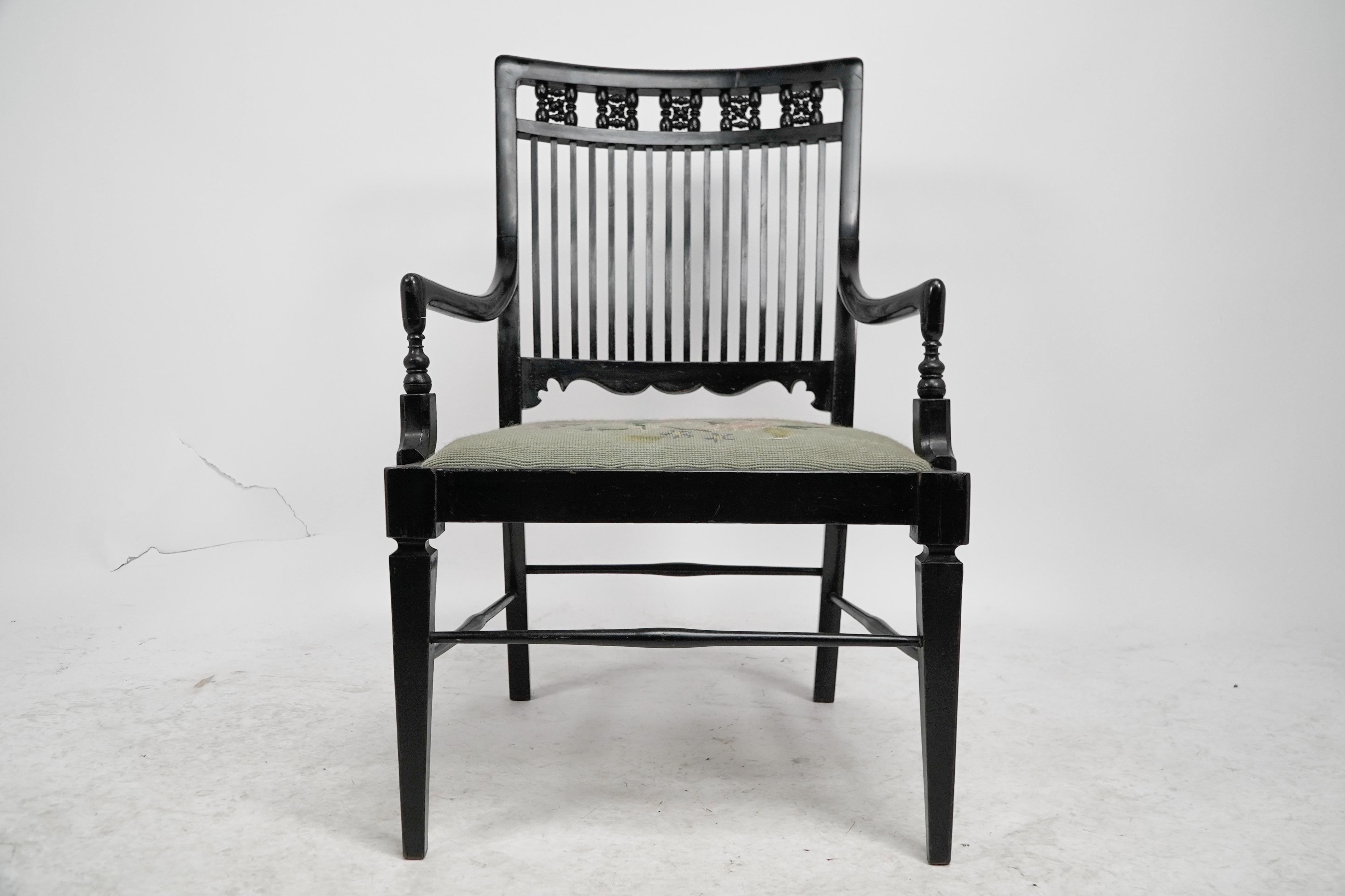 Liberty & Co An Aesthetic Movement ebonized Moorish low armchair with a shaped back with mashrabiya turnings to the head rest and tapestry seat