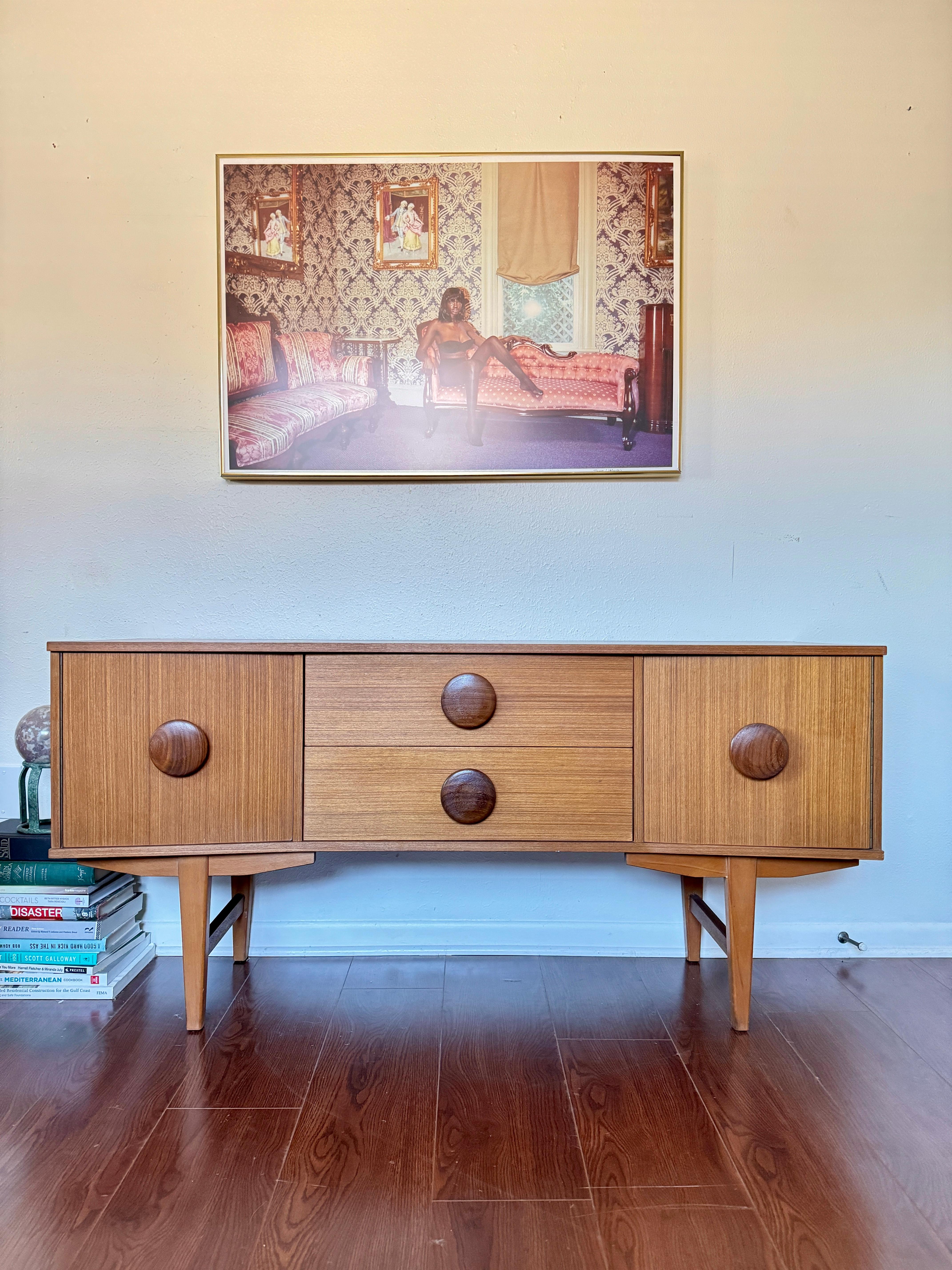 An MCM petite sideboard with button pulls, circa 1960s. Refined by its curve that gives it elegance and circular pulls that gives it a modern edge, this piece can go in any style home. Overall in very good original condition. Some discoloration on