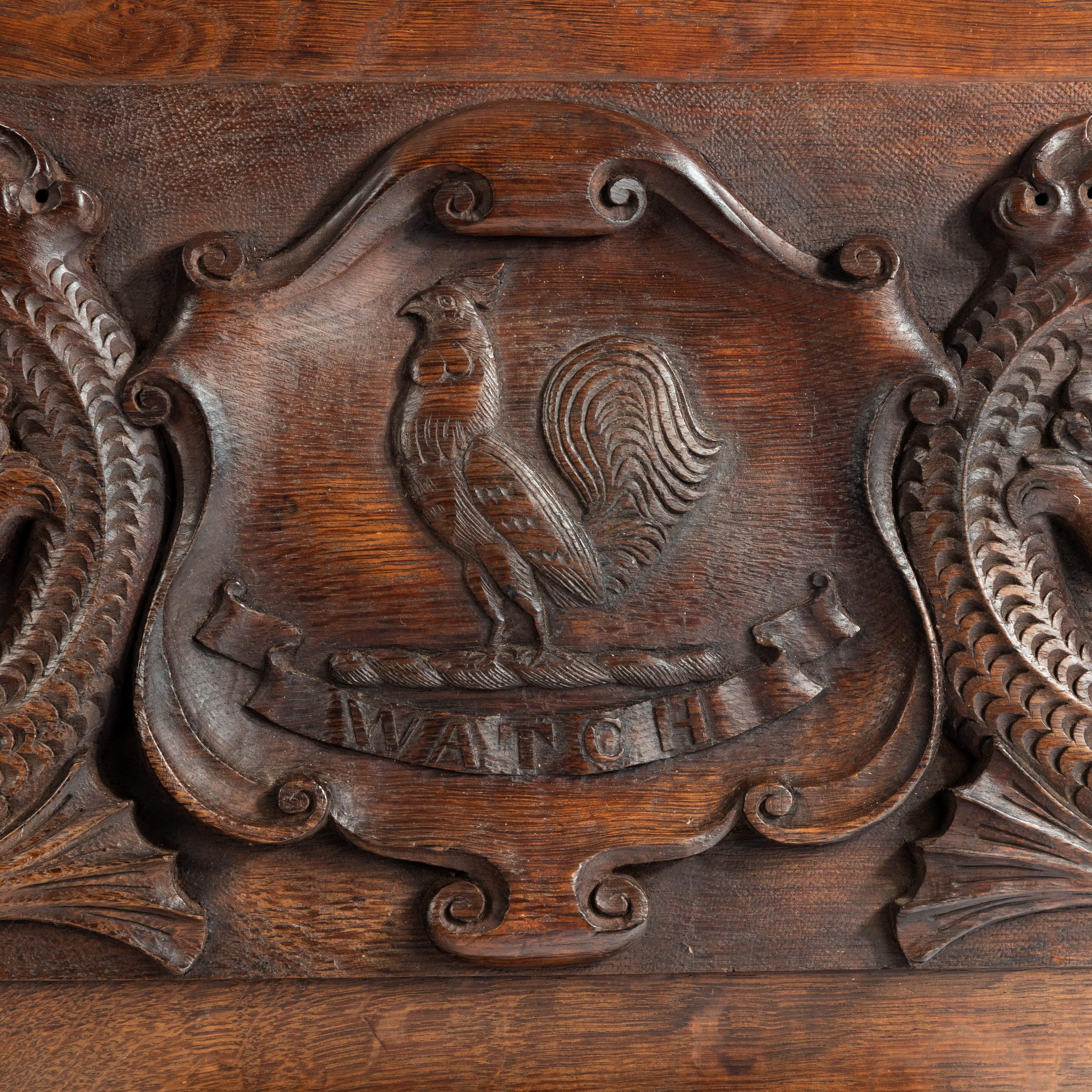 An oak barge board with the Insignia of Admiral Sir G.E. Patey, of rectangular form with a central escutcheon enclosing the arms of the Patey family; a cockerel and a ribbon bearing the word WATCH, flanked by dolphins with scrolling tails. This