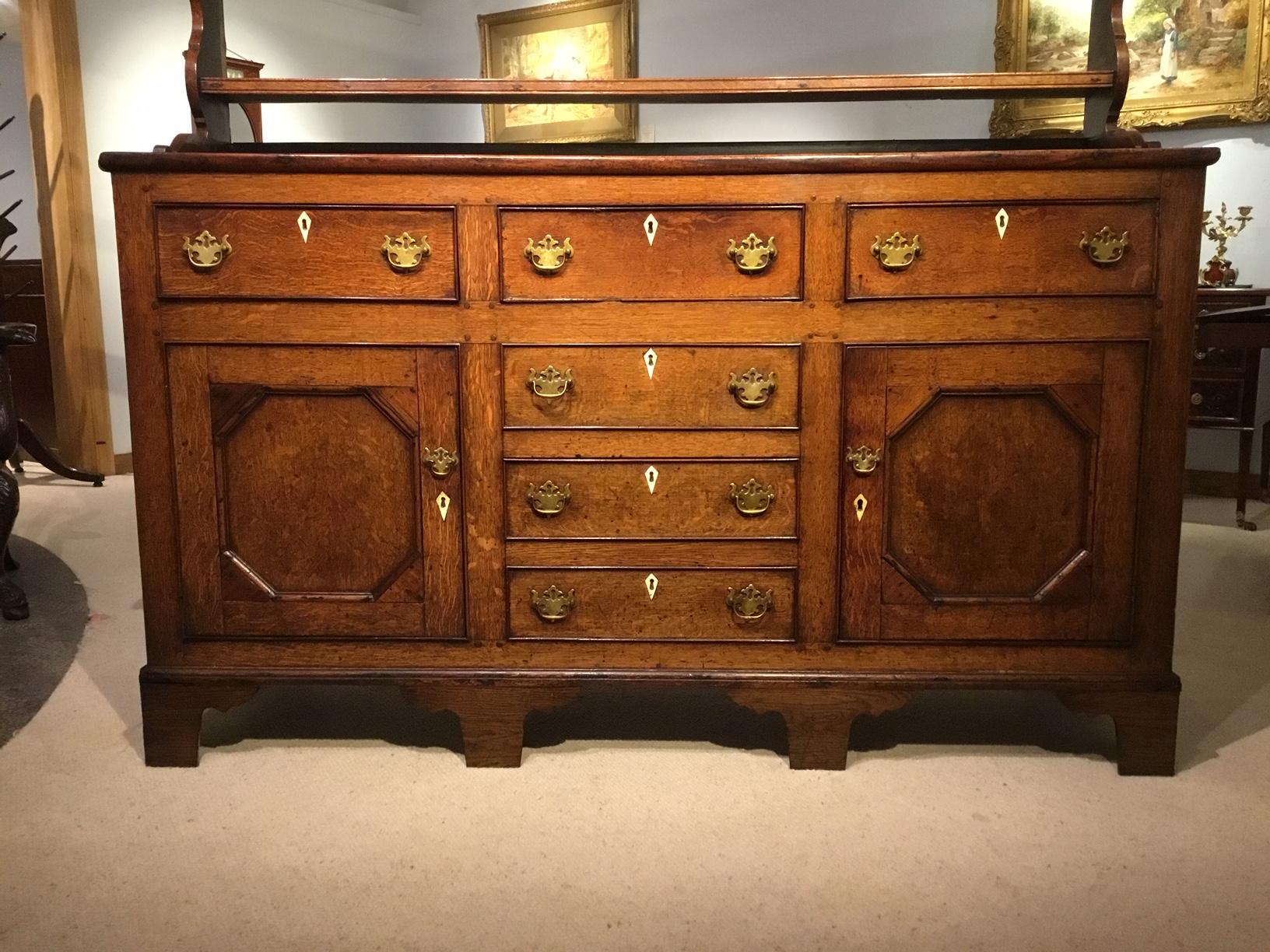 An oak early 19th century welsh dresser and rack. Having an upper rack section with three shelves and shaped ends. The lower section with a three plank oak top above an arrangement of six drawers and two cupboards with brass swan neck handle and