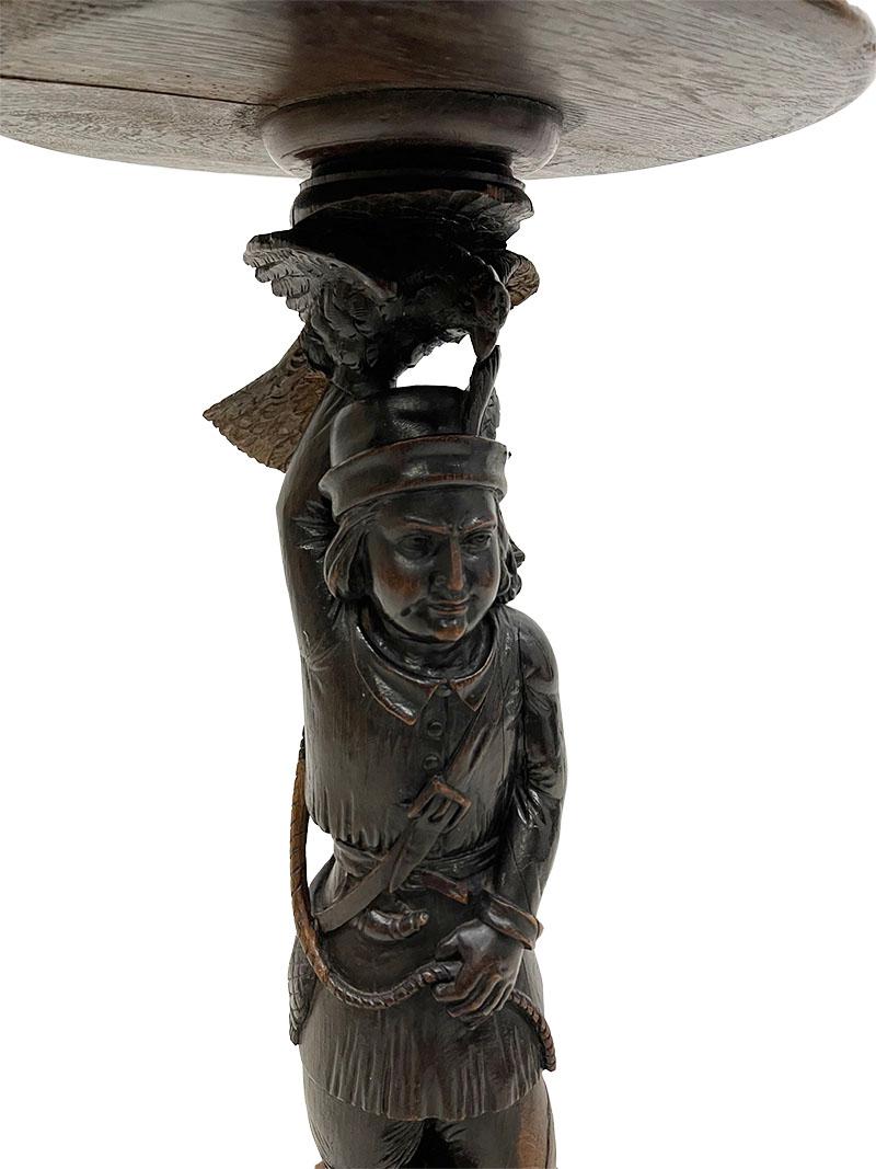 An oak falconer's pedestal or plant stand

An oak plant table, pedestal with a round base, raised on three semi-circular feet. In the center is a hand-carved wooden figure of a falconer holding a bird of prey, with a round platform on top. One tip
