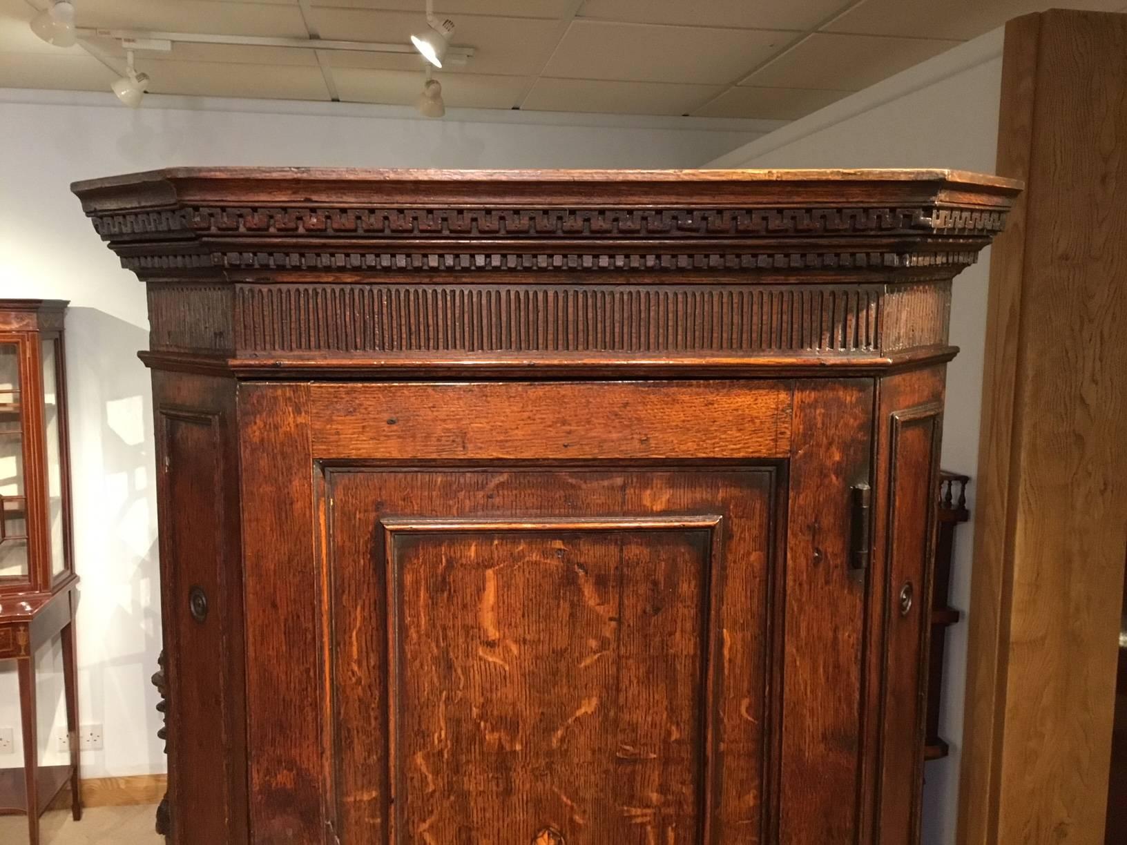 An oak George III Period antique corner cupboard. With a Greek key and dentil moulded cornice above the rectangular oak panelled door with central shell inlaid paterae, flanked by angular ends with turned roundels and opens to reveal a shaped