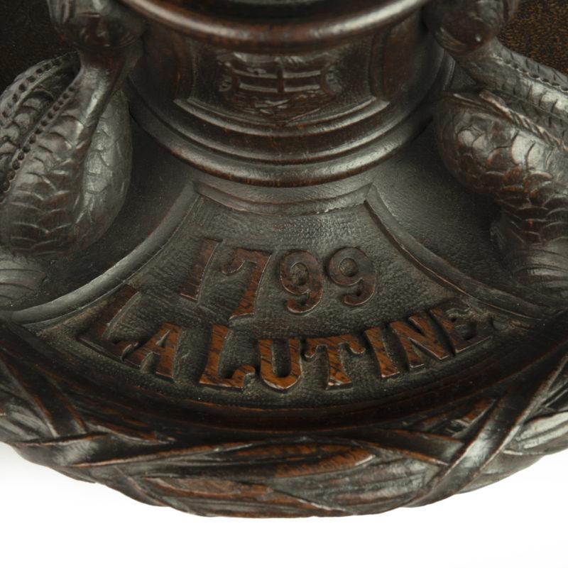 This large and historically interesting inkwell, or standish, is carved from timber recovered from the wreck of H.M.S. Lutine.  It has a central inkwell, with a bud and oakleaf cover, supported by three dolphins within a circular dish within a