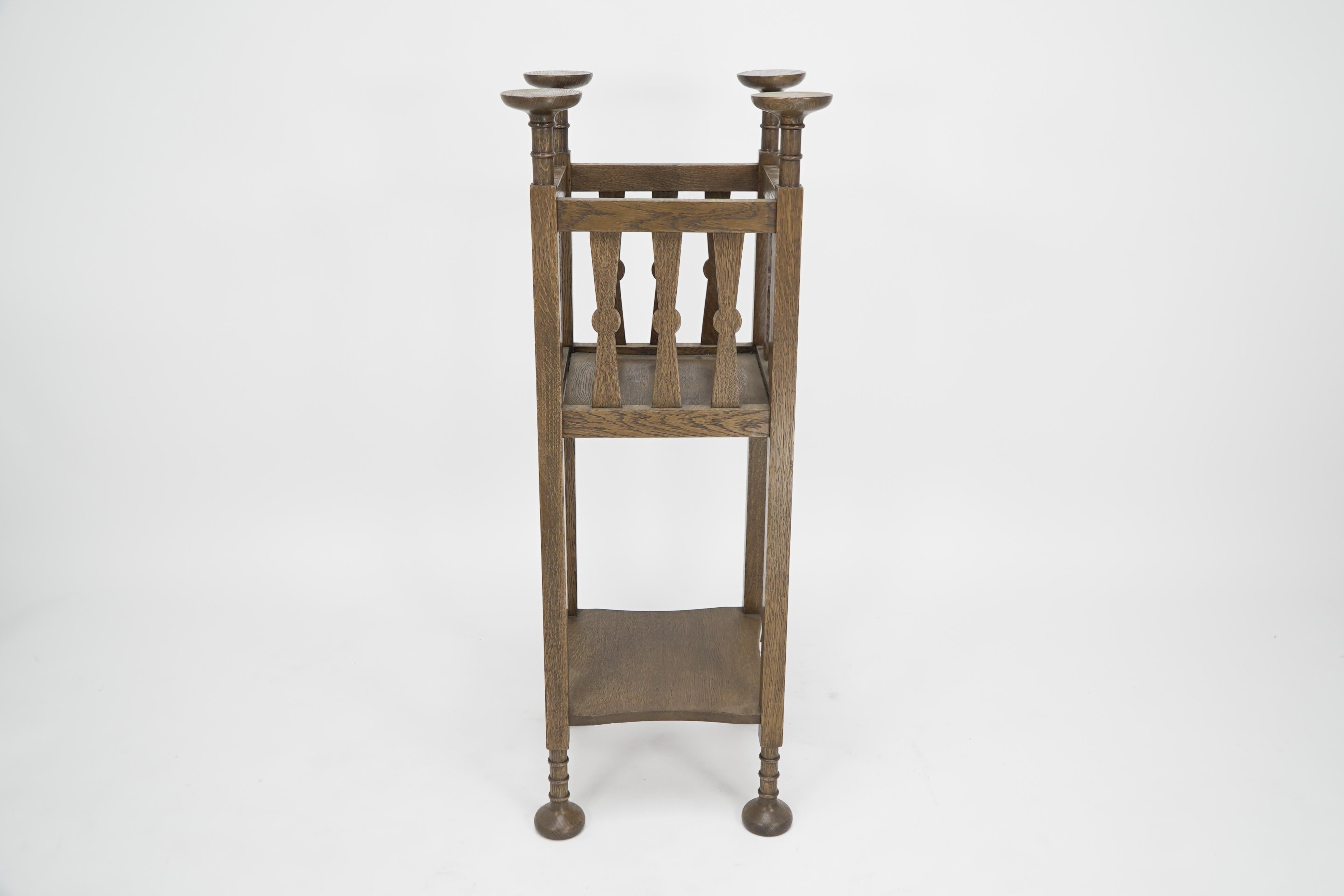 Shapland & Petter. An Arts & Crafts oak plantstand with Voysey style discs finials, and lollipop style uprights to the upper section, on square legs united by a lower shelf. with turned Thebes-style feet.

