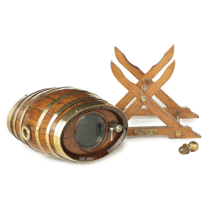 An oak spirit barrel made from H.M.S. Victory timber, 1890, comprising a small coopered cask with brass rings, a central tap and stopper, and glass ends, inscribed ‘made from the piece of one of the timbers of the cabin from HS Victory, struck by a