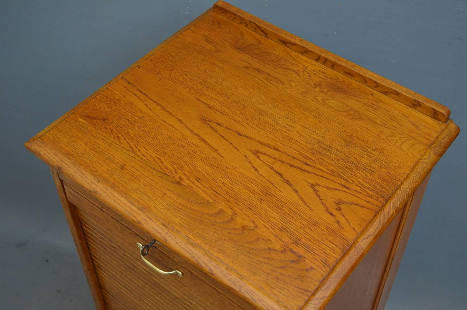 Sn4271, turn of the century oak, tambour fronted filing cabinet of soft color, having moulded top and panelled sides above tambour front enclosing nine drawers, fitted with original working lock and key, standing on plinth base. This antique filing