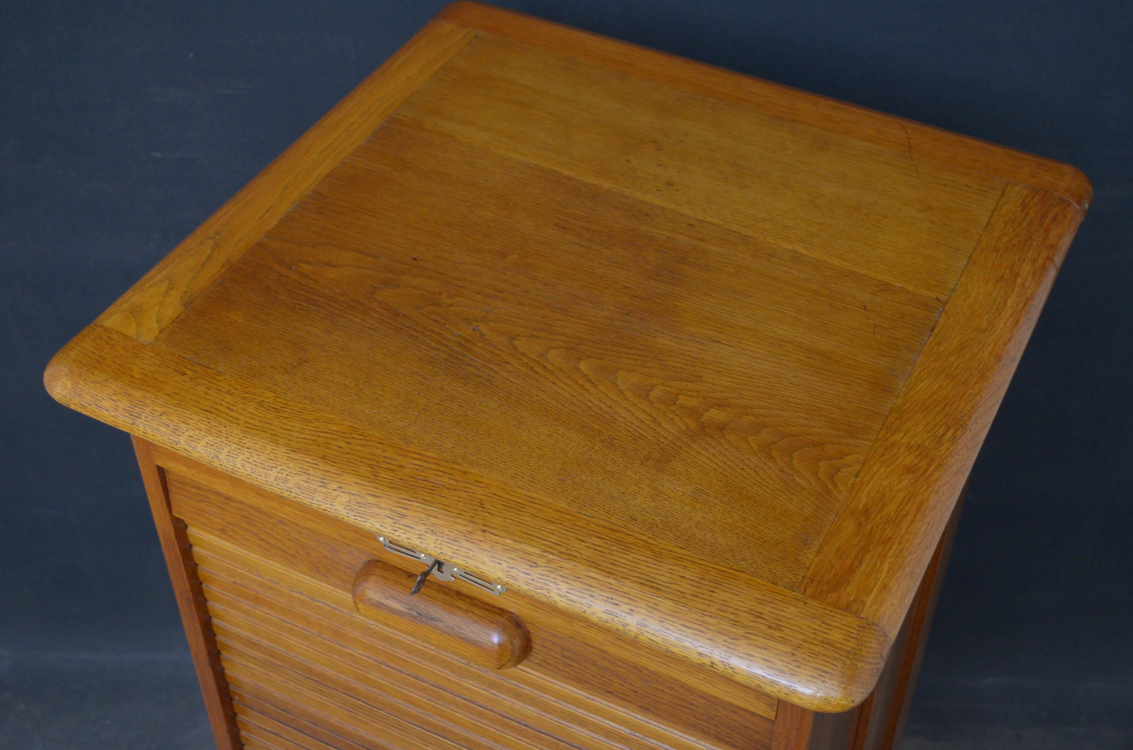 Sn4818, turn of the century oak, tambour fronted filing cabinet of soft color, having moulded top, panelled sides and tambour front enclosing 9 drawers, fitted with original working lock and key, standing on plinth base. This antique filing cabinet
