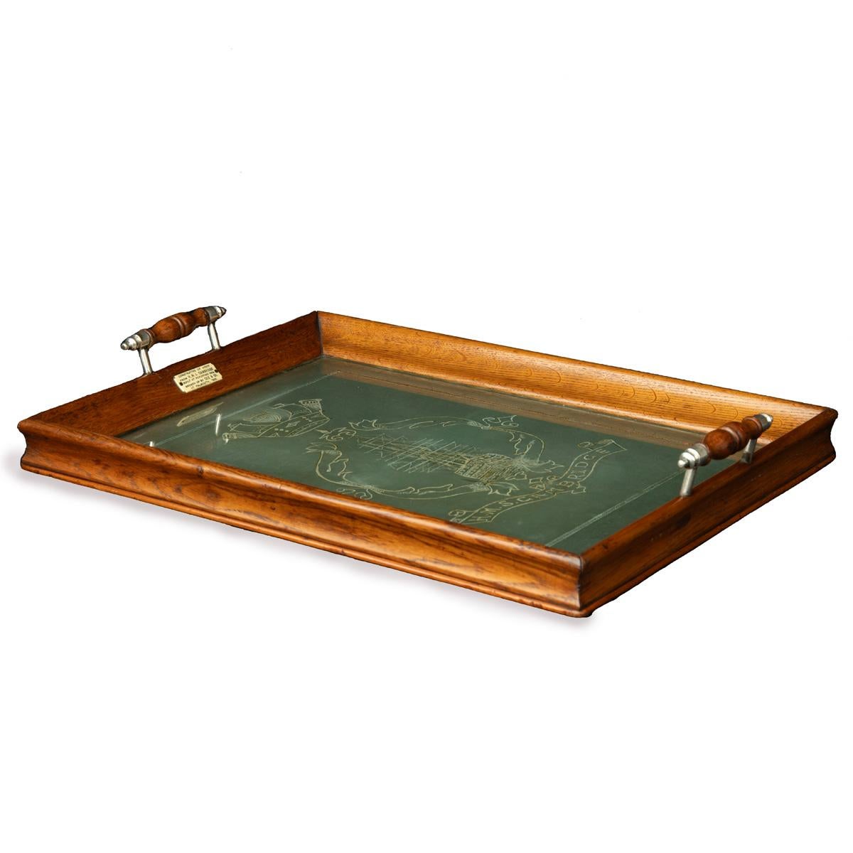 An oak tray from H.M.S. Cambridge, of rectangular form, the carrying handles with turned silver plated ends, decorated in cream on a green ground with a ribbon cartouche enclosing a ship of the line, all below a naval crown and above the legend