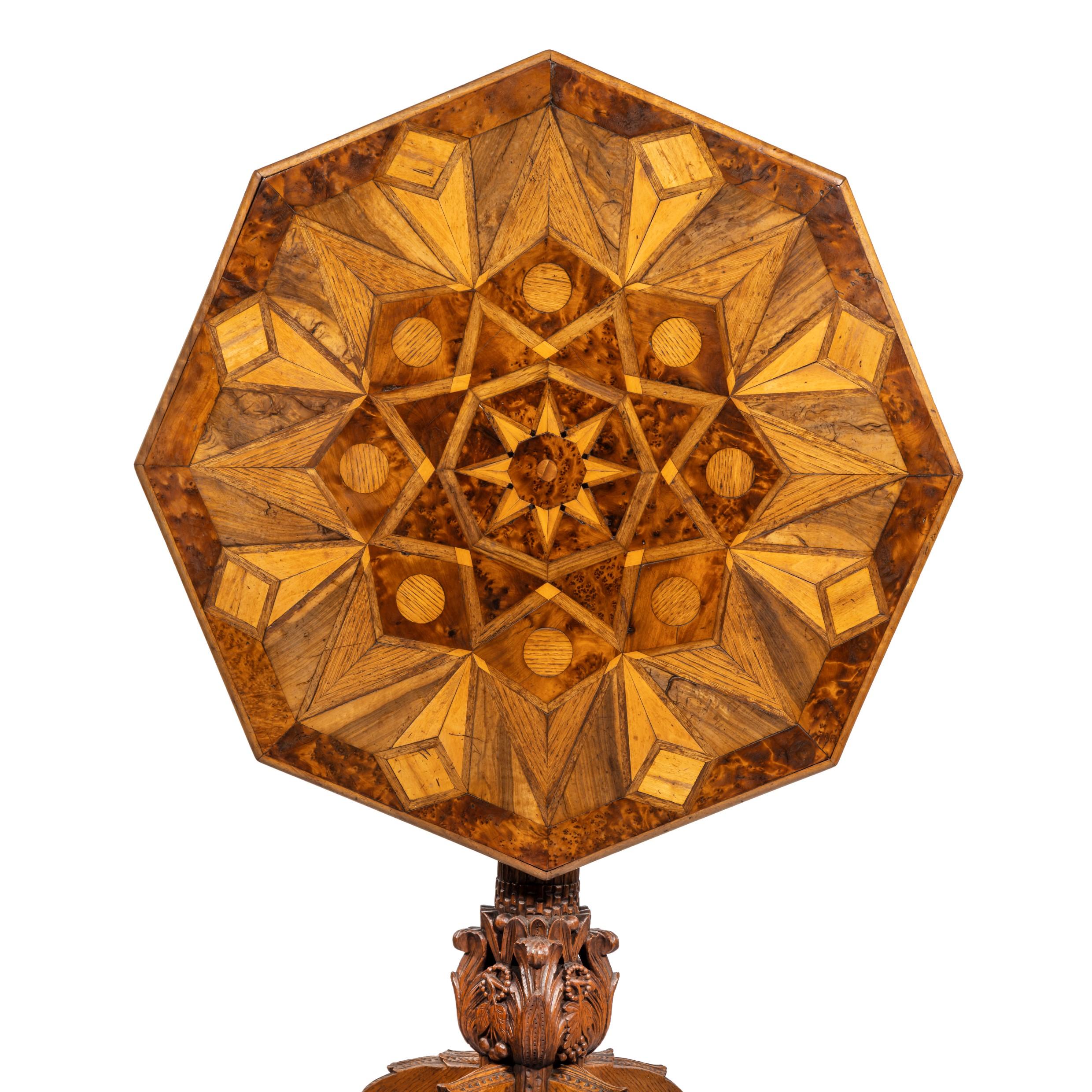 An octagonal indigenous specimen wood marquetry table, the tilt top inlaid on both sides with triangles and diamonds in an overall star design, the woods include yew, oak and elm, on a carved classical column base with four cabriole legs. British,