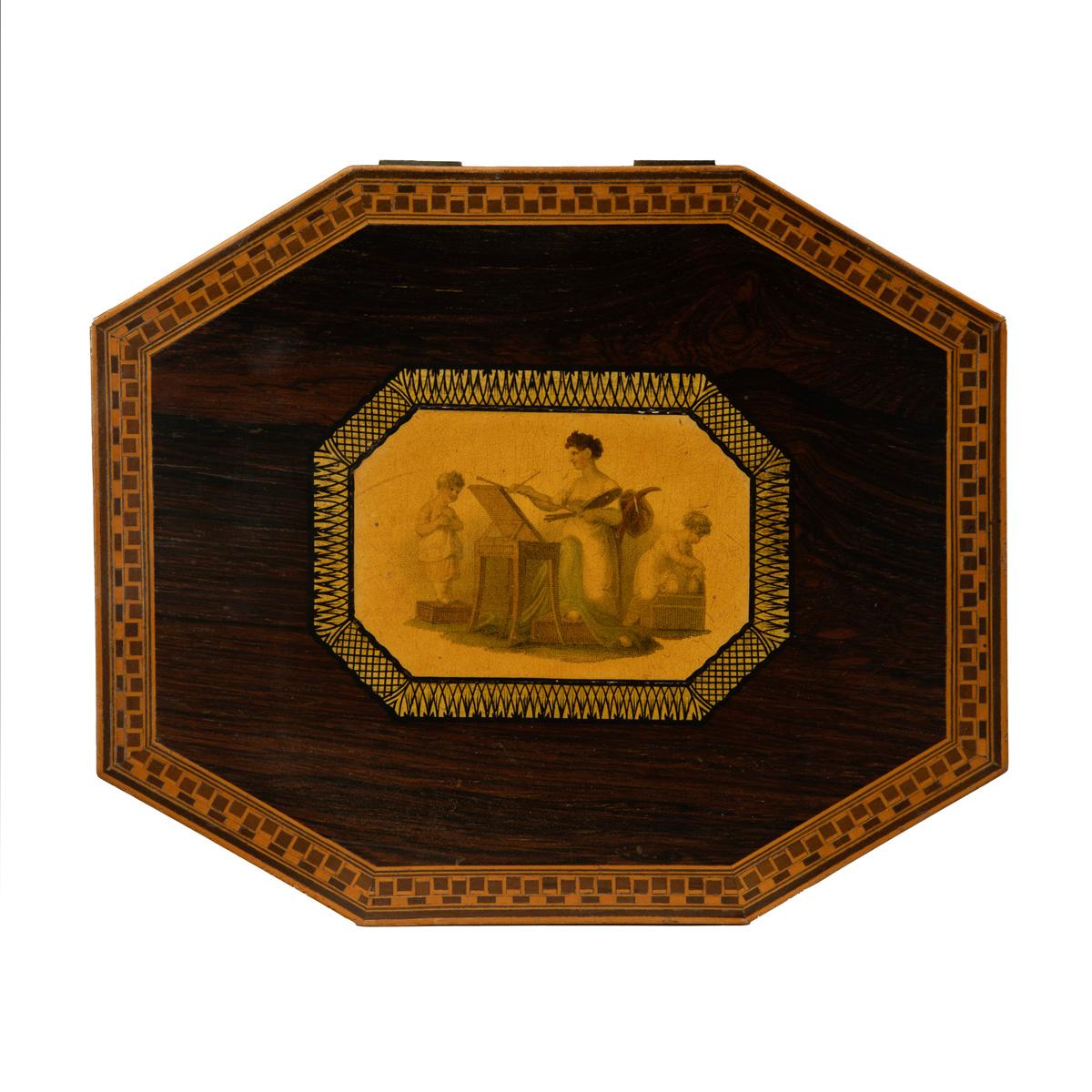 An octagonal Regency rosewood card box, the hinged lid with a central cartouche showing a classical lady painting a child while another child plays on a stool, all within a gilt and black penwork border, with boxwood stringing and inlays, the pale