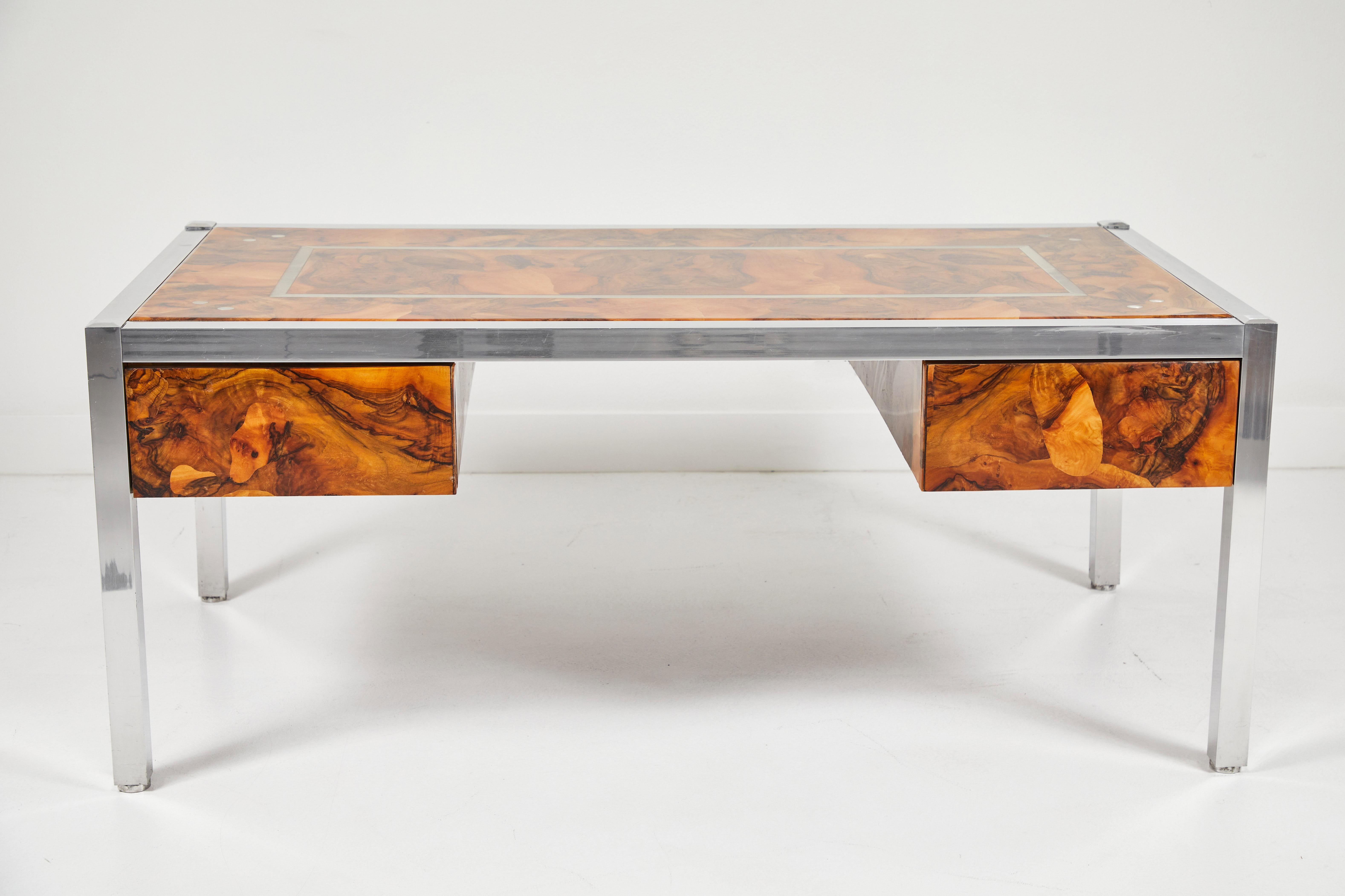 A striking olive burl desk with aluminum legs and accents. A layer of resin encapsulates the desk revealing the distinct patterns in the burl wood. The desk has 2 drawers, one on either side and rests on aluminum legs. A perfect accent for any