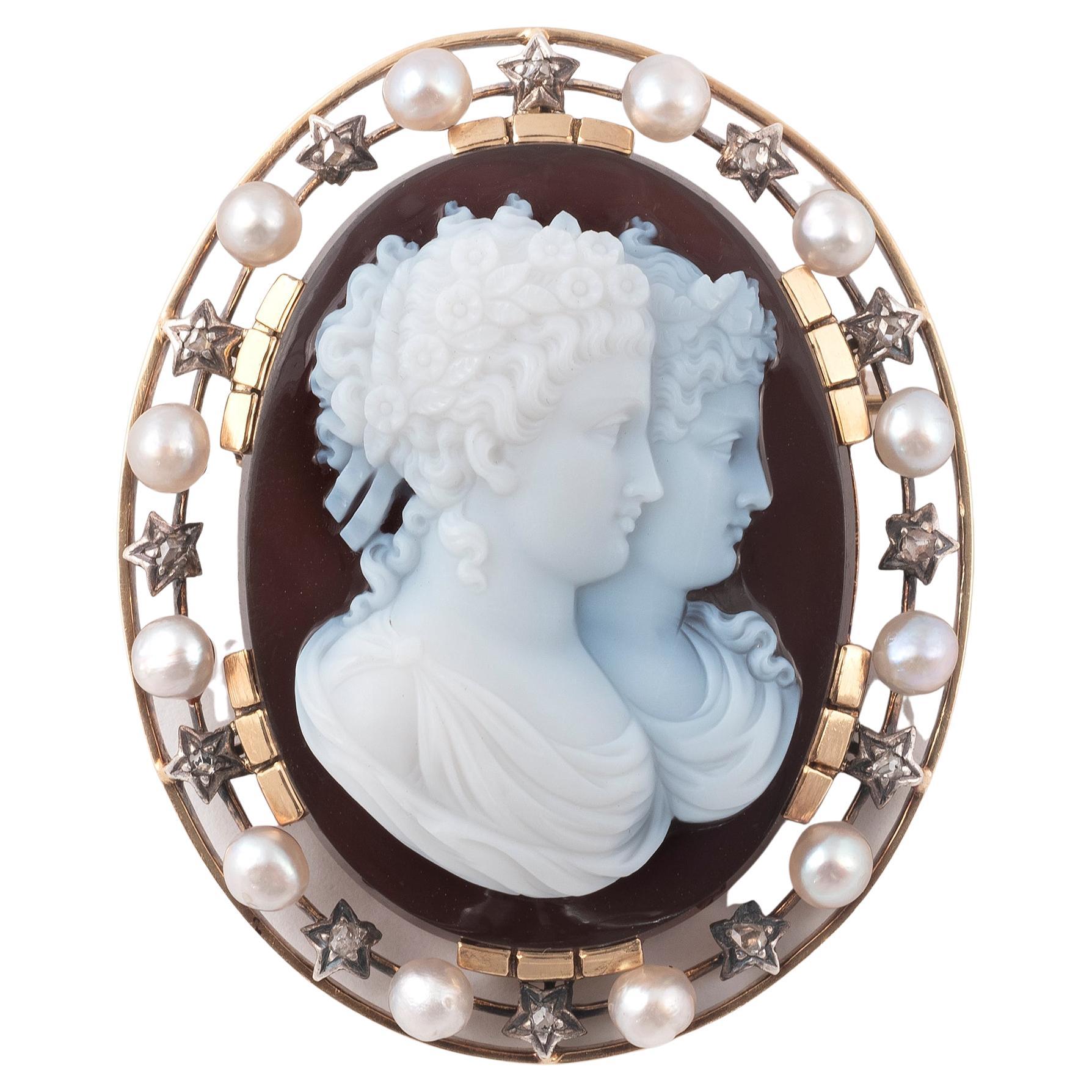 The oval onyx cameo, carved to depict the double portrait in profile, within rose diamond and pearl border, mounted in silver and gold
Length 6cm
