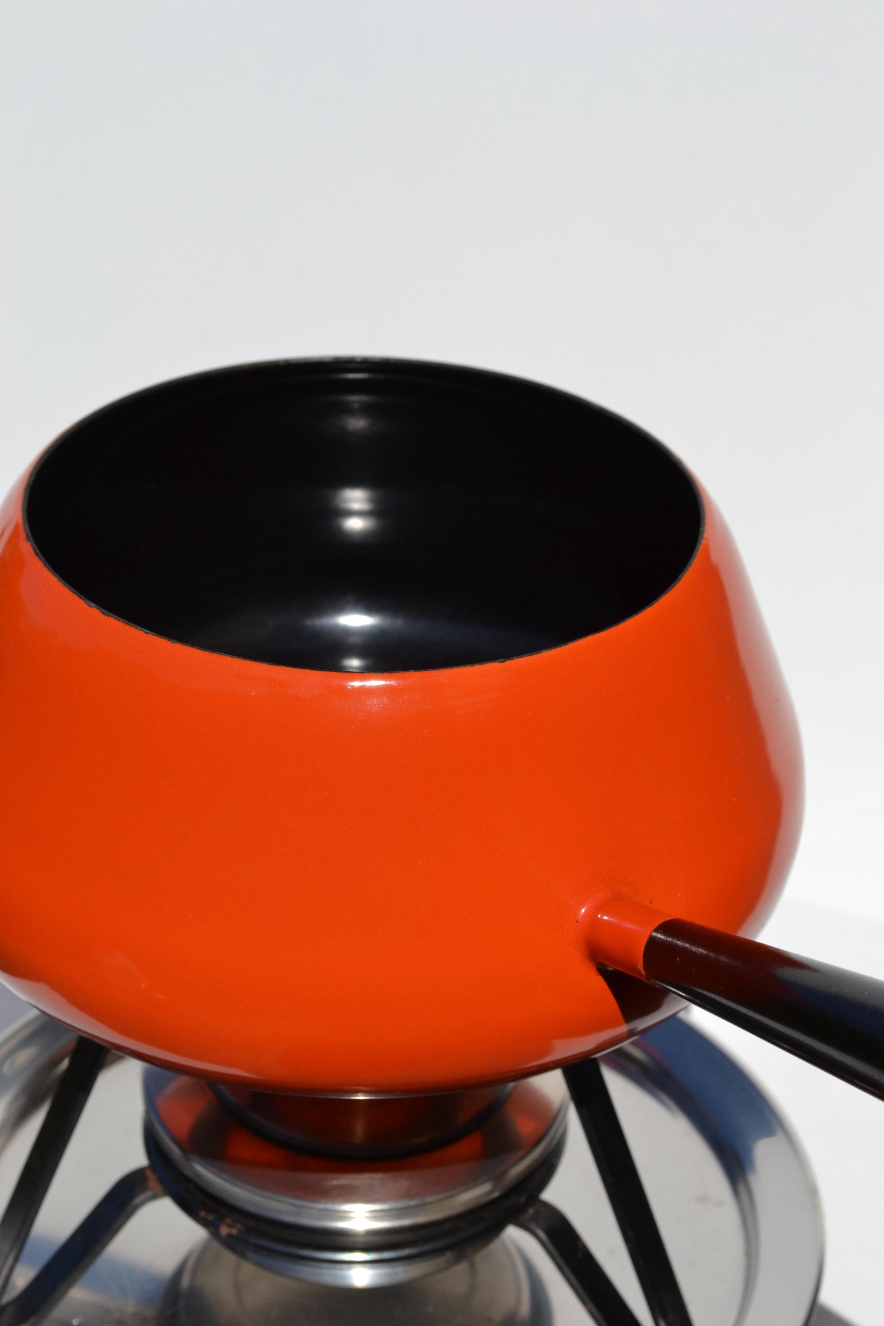 Ein wunderschön erhaltenes komplettes Fondue-Set, das in den 1960er Jahren in der Schweiz von der bekannten Marke Spring hergestellt wurde.
Dieses seltene Modell verfügt über einen leuchtend orangefarbenen Emaille-Topf, einen eleganten verchromten