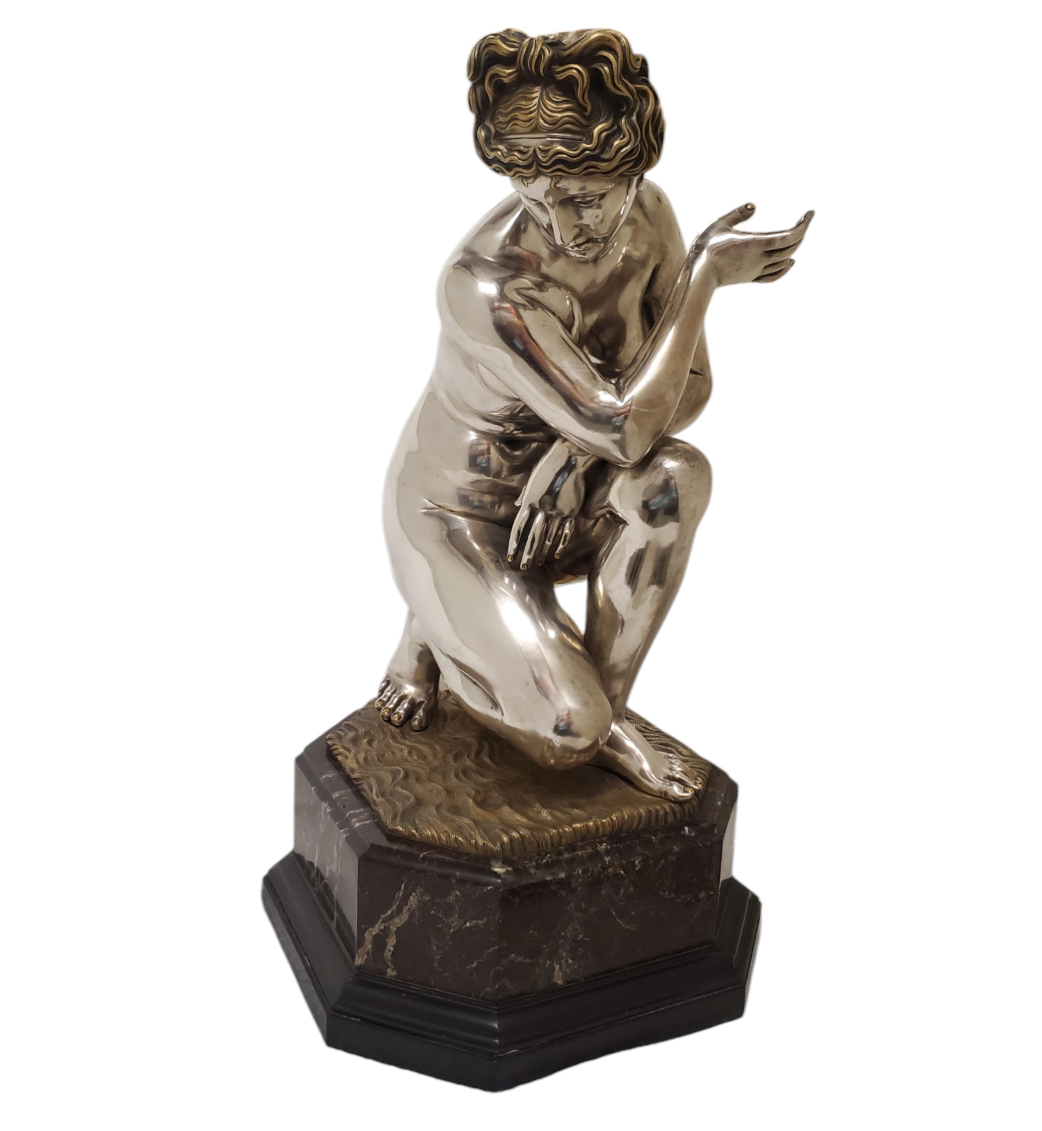 Questa squisita scultura della metà del XIX secolo presenta una donna nuda in bronzo argentato con accenti dorati. La figura femminile incarna grazia e fascino, ricordando la dea Venere. La donna è raffigurata in posizione inginocchiata con una