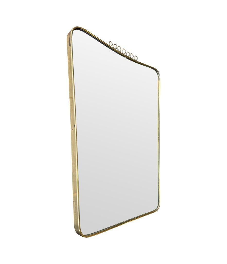 Miroir italien original des années 1950 à encadrement en laiton, attribué à Gio Ponti, avec des détails de gribouillis en laiton sur le dessus. Avec la plaque miroir d'origine et le dos en tôle pleine.