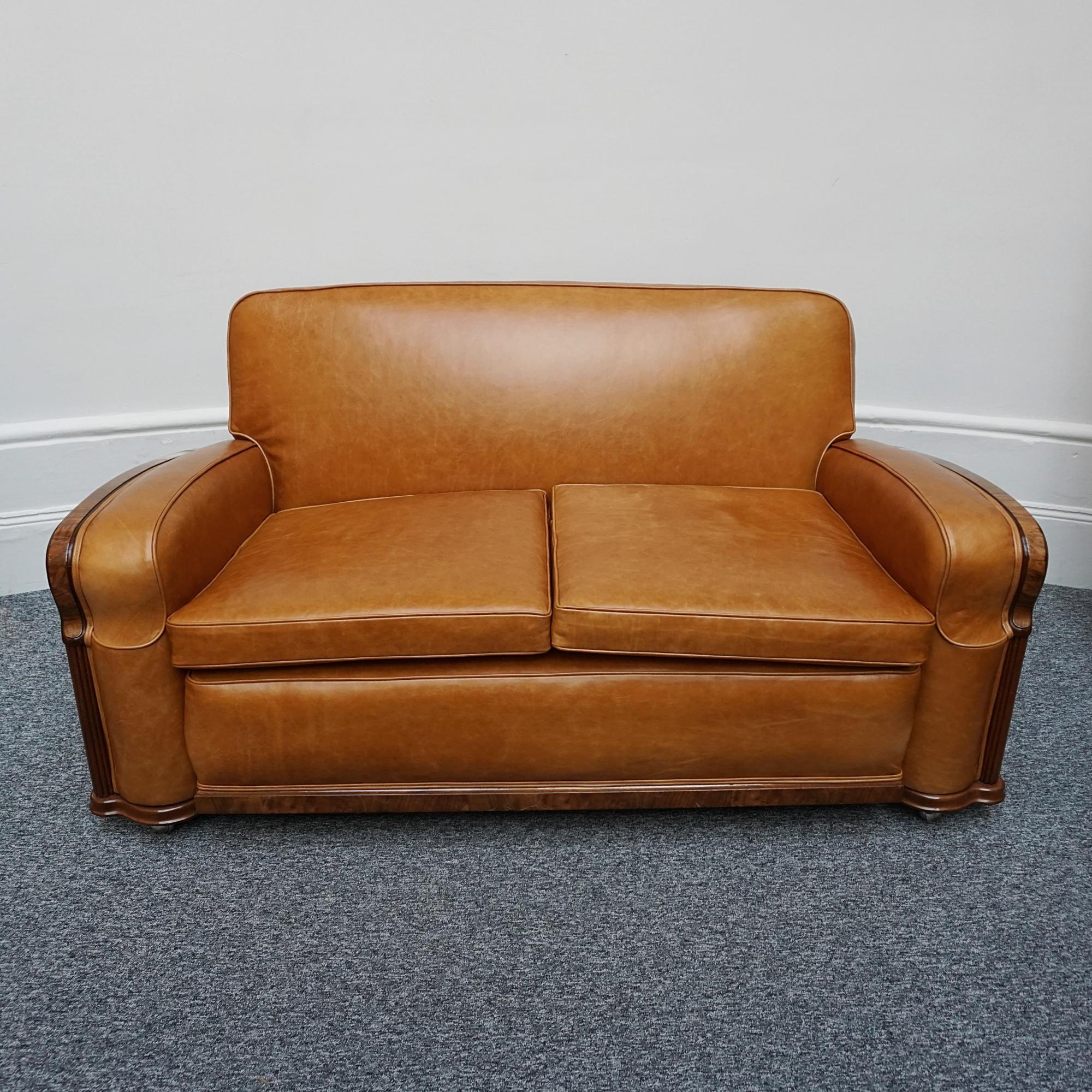 An Art Deco Club Sofa. Burr and figured walnut veneered throughout with burr walnut banded arms and scrolled detail. Re-upholstered in brown leather. 

Dimensions: H 79cm W 168cm D 71cm Seat H 49cm W 123cm D 61cm

