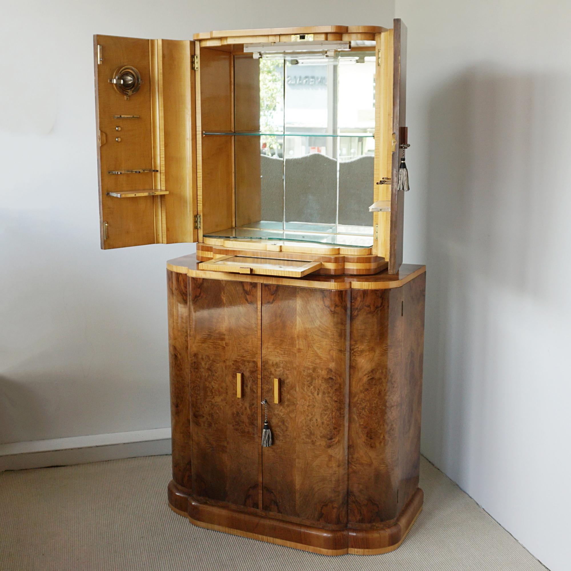 An Art Deco cocktail cabinet. Burr walnut veneered with satin birch banding with an upper mirrored lit interior and integral pull out mixing tray. Lower compartment with extensive bottle storage and two upper drawers. Satin birch interior