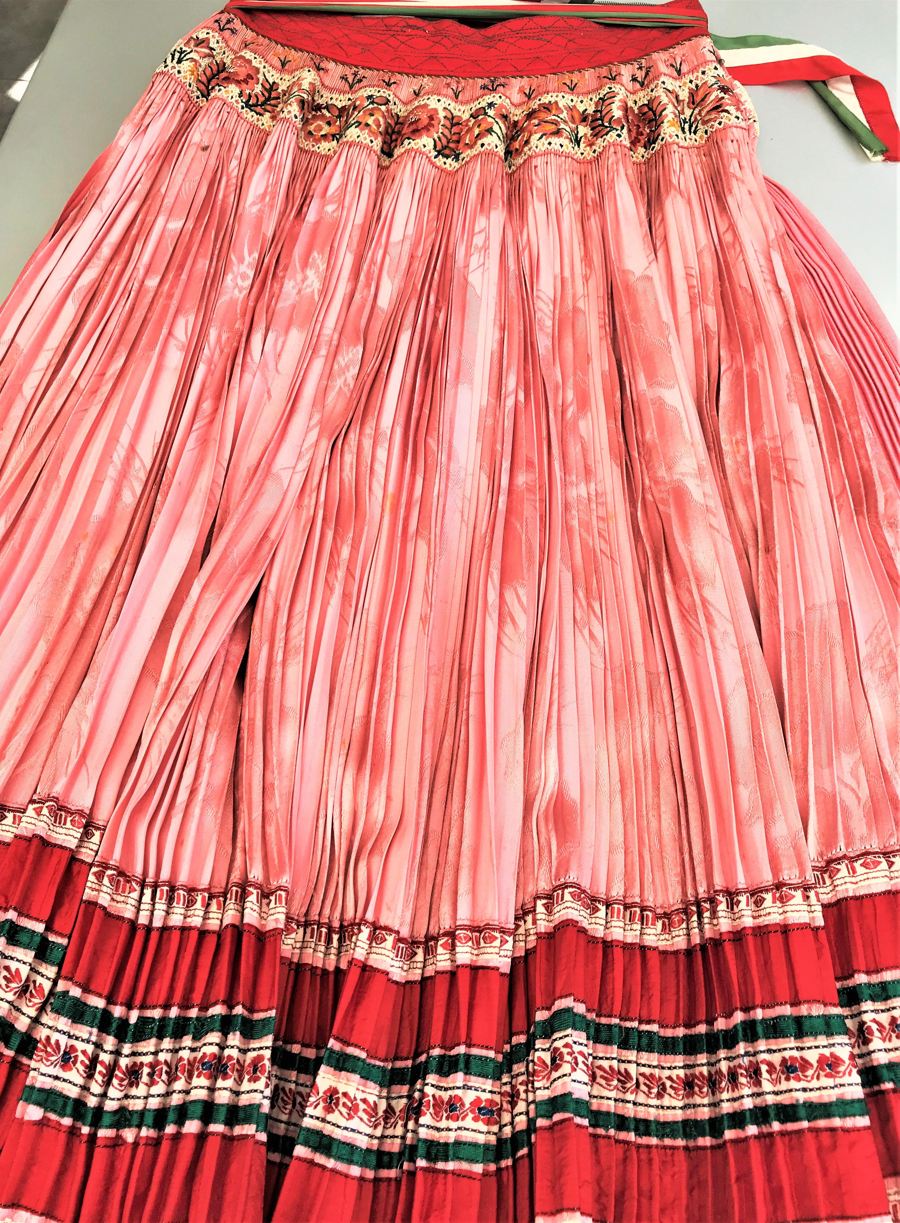 Jó napot kivanok!
A beautiful pleated skirt in pink with a hand-embroidered border over the hip. -Traditionally, the matching apron is worn over the one-colored front part.
My most beautiful, finely pleated apron with 2 wide hand-embroidered