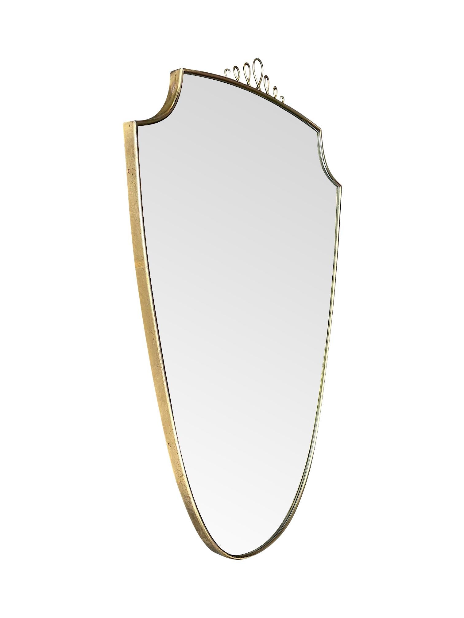 An original 1950s Italian brass shield mirror in the style of Gio Ponti with pretty central decorative detail. Mounted on solid wood back.