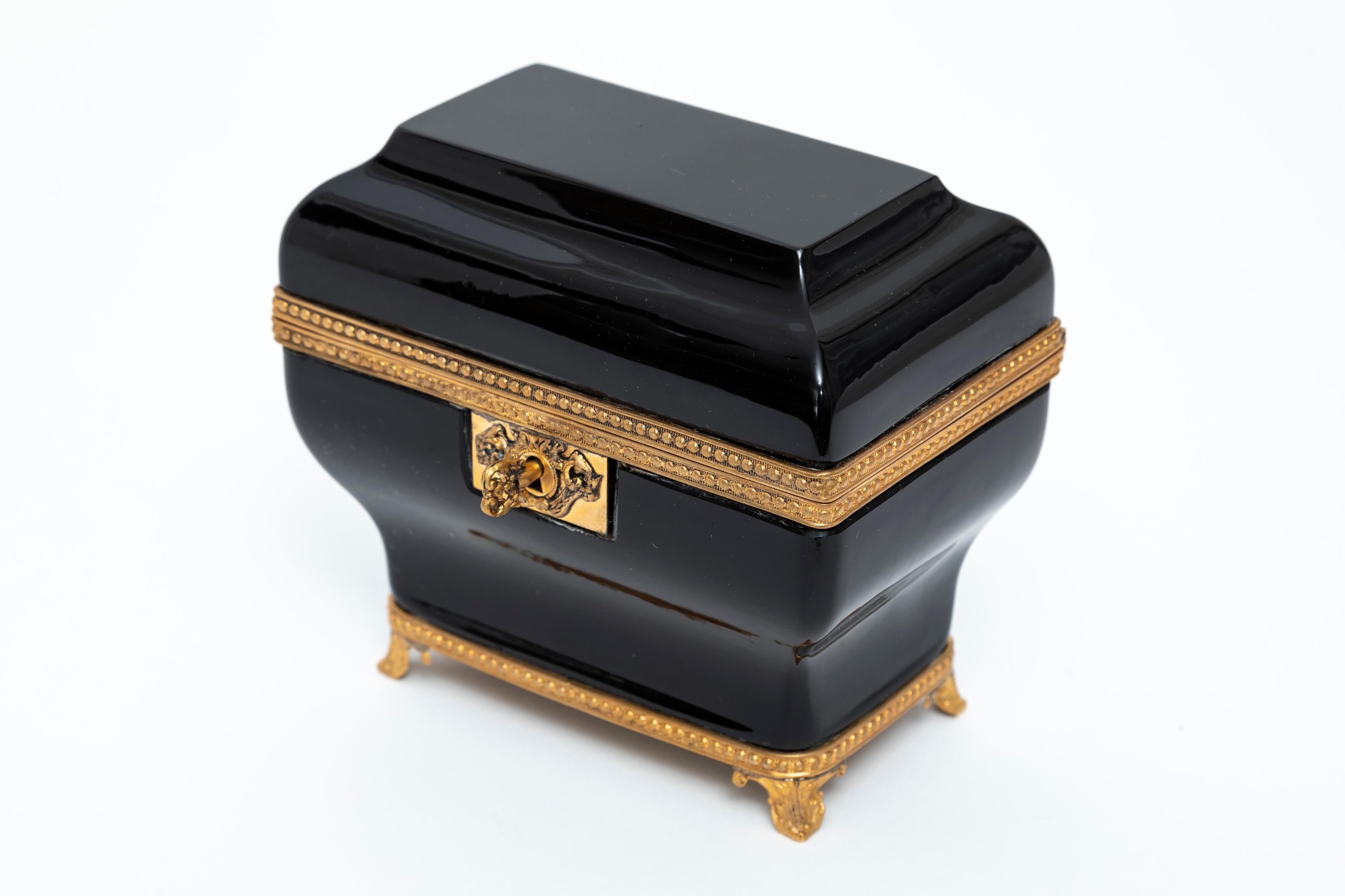 Inusual joyero de cristal de amatista negra montado en ormolu, atribuido a Baccarat.  Bellamente abisagrada en el centro, con una montura de cuentas de bronce dorado, así como patas de bronce dorado.  El cristal es dese y muy probablemente producido
