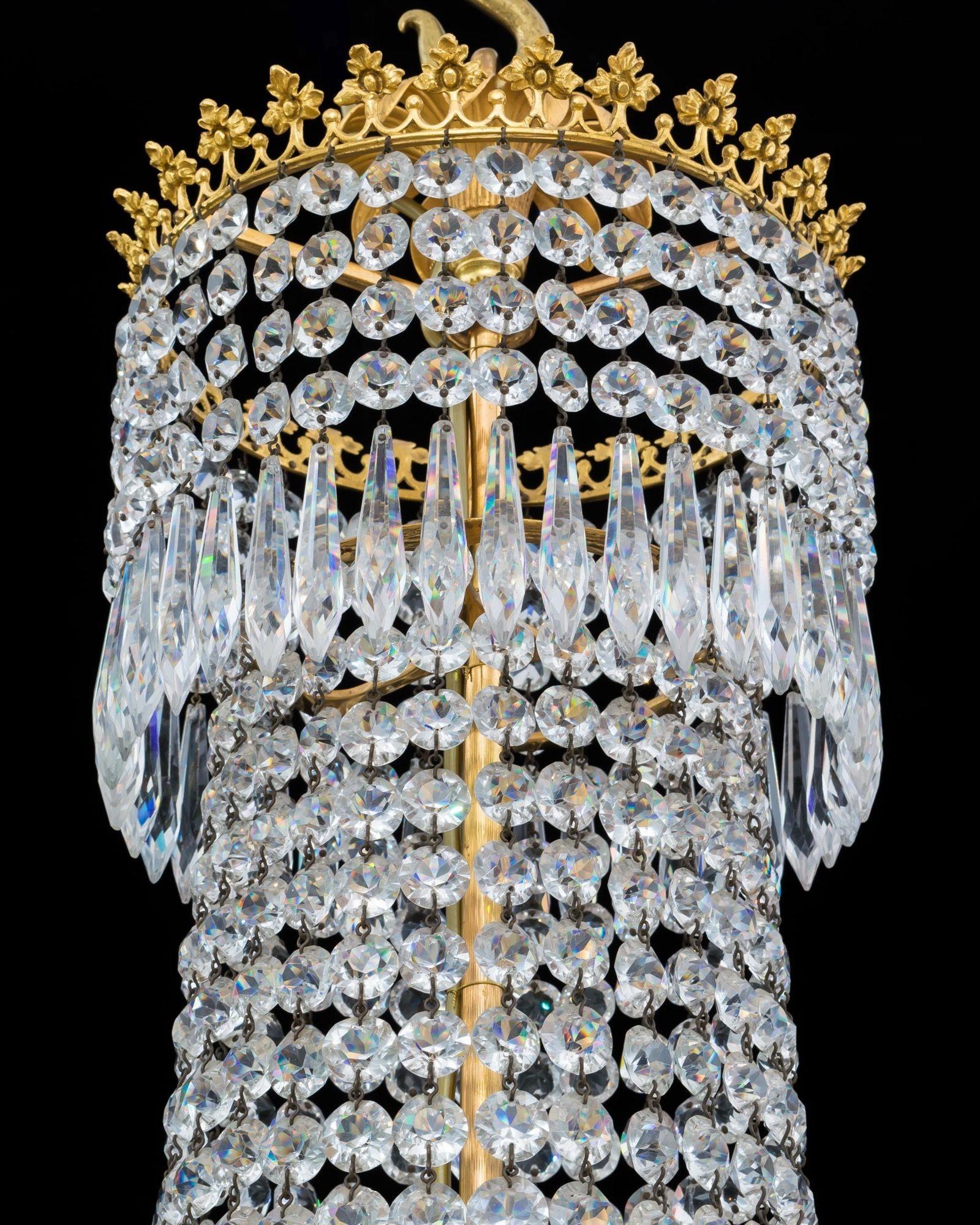 The chandelier of classic tent and basket design, mounted with ornate motif bands supporting graduating spangles cascading to the main ring, issuing eight scroll arms supporting diamond and radial cut candle nozzles, the chandelier hung with icicles
