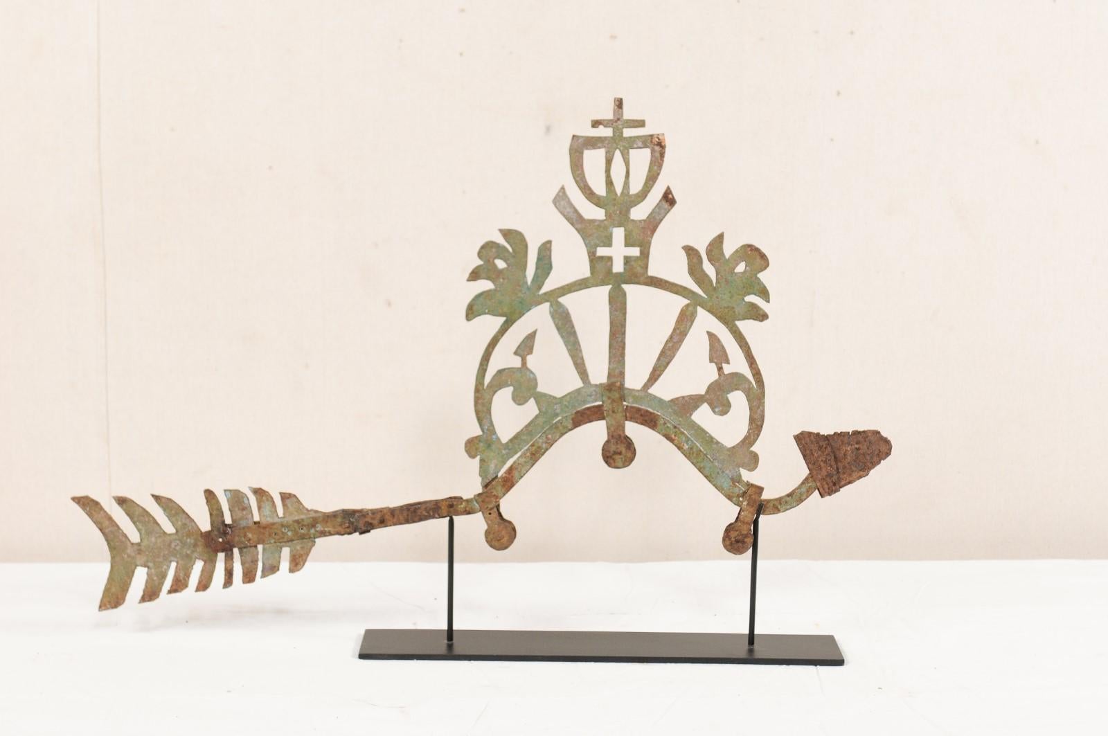 An ornamental bird fragment from the 19th century presented on stand. This antique decorative metal piece from Indonesia features a bird with crown and cross motif at its center, which has been displayed on a custom black iron stand. The old metal