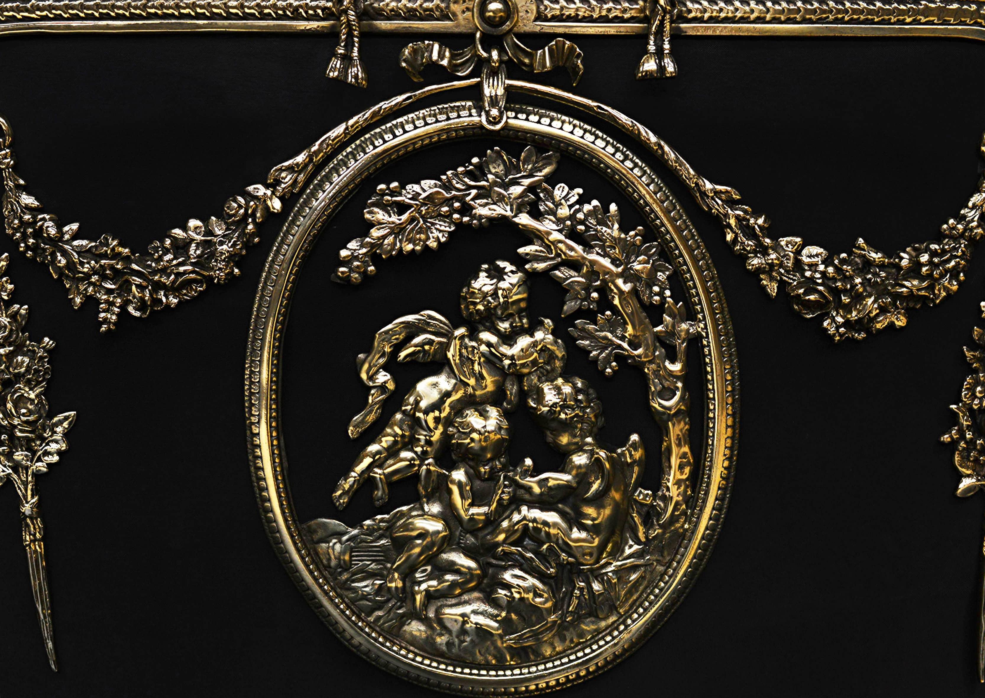 An ornate French Rococo brass firescreen. The hoofed feet surmounted by stiff acanthus leaves and guilloche pattern to outer frame, with rope handle above. The black mesh adorned with swags and central plaque featuring putti and foliage. French,