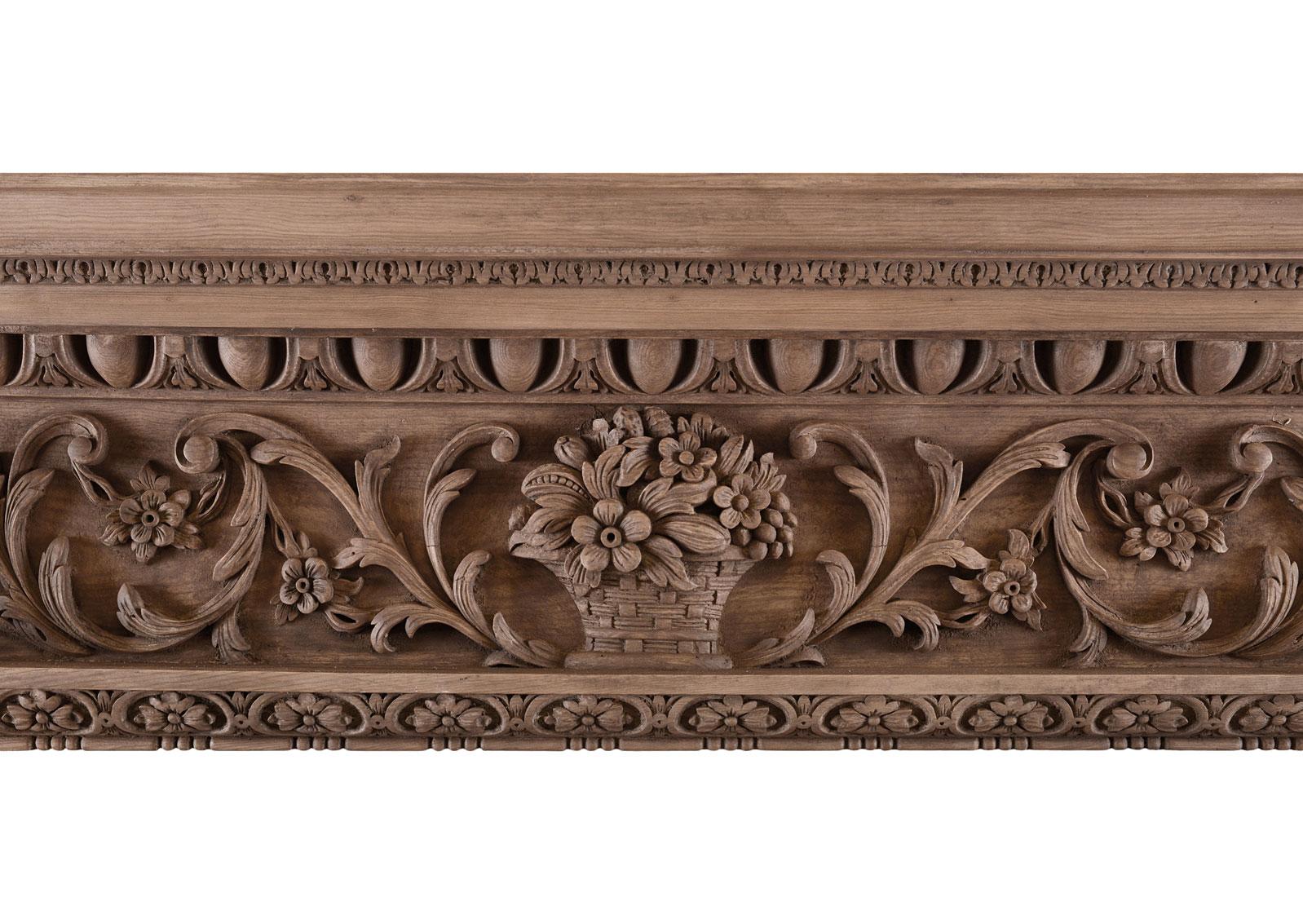 A heavily carved English timber fireplace. The jambs with inlaid panel of carved fruit and flowers surmounted by carved brackets with cartouche, flower and scrolls. The frieze with basket of flowers to centre flanked by scrolled leaf work. The shelf