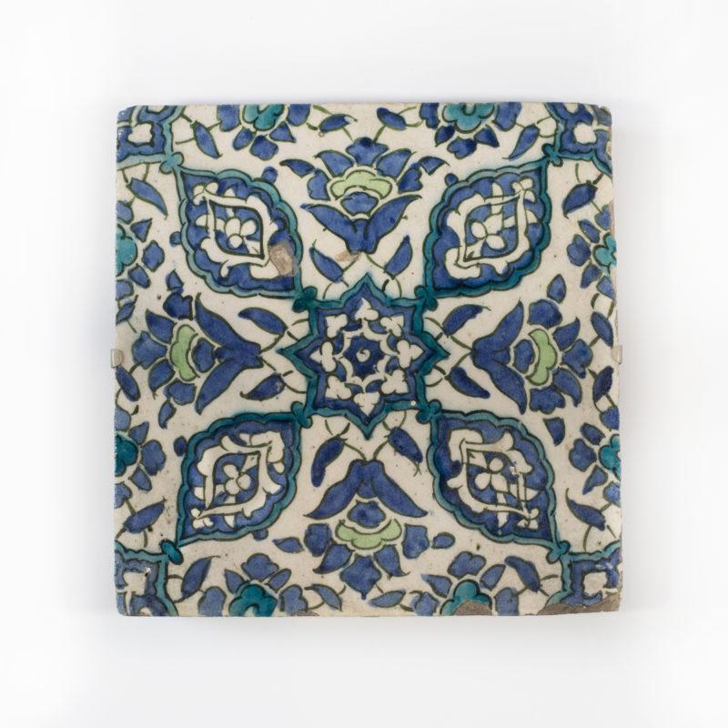 An Ottoman Empire Damascus square tile, late 16th century, the glazed fritware body painted in underglaze green, blue, turquoise and black with four lobed medallions and four split palmettes centred on an eight-pointed floral star, mounted.