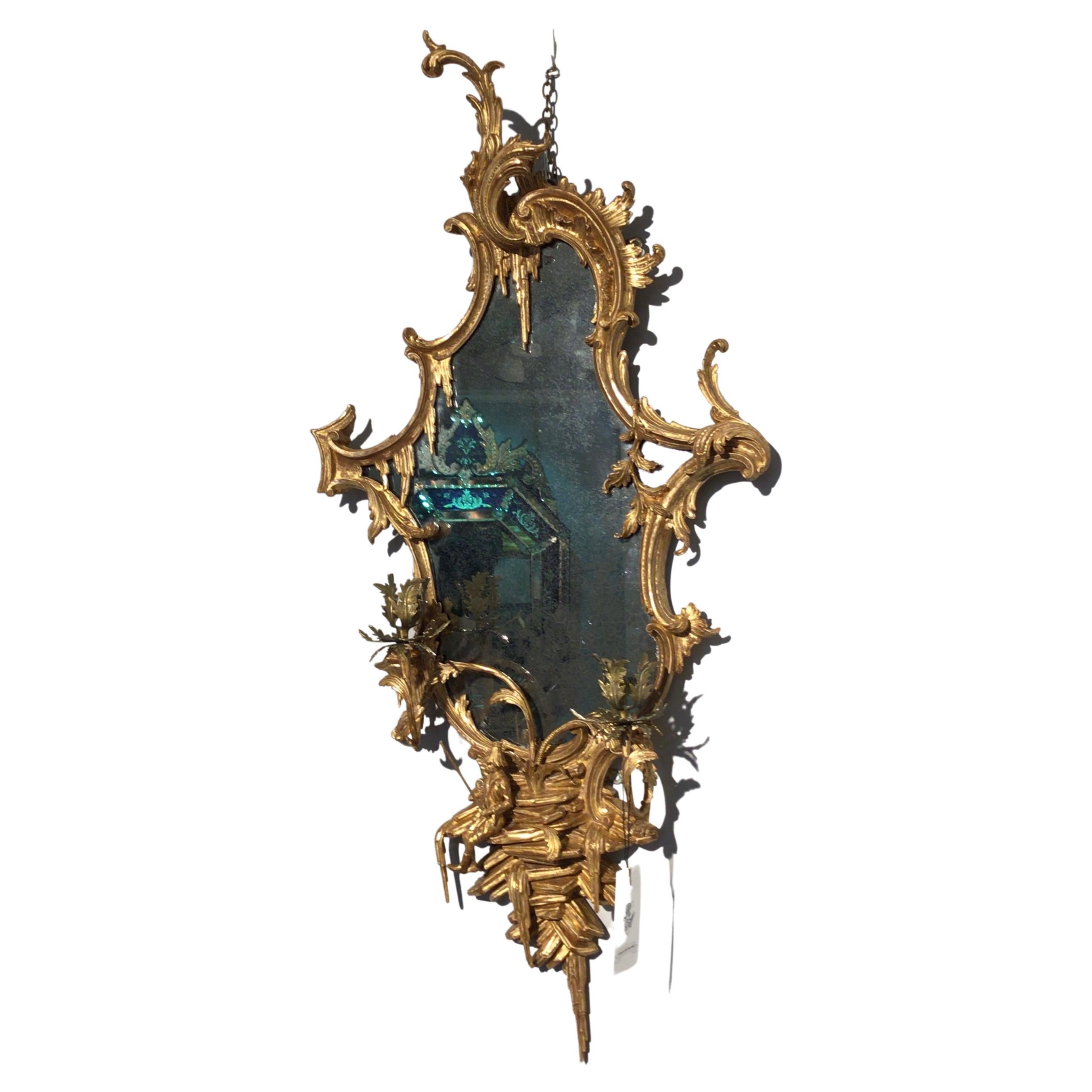 An outstanding Chinese Chippendale carved giltwood girandole, this lovely and entrancing piece is carved in the chinoiserie style, the asymmetric form echoed by the skewed setting of the two single candle arms to either side of the original mirror