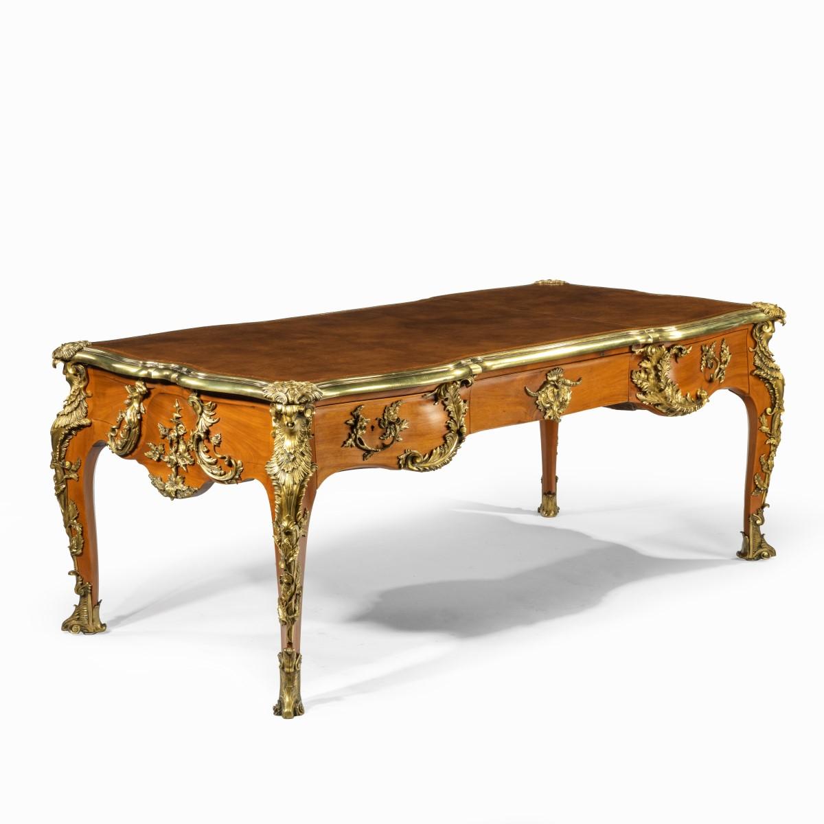 An outstanding Louis XV-style mahogany bureau plat after a model by Jacques B. Dubois, from the estate of Phyllis McGuire, the shaped leather-inset top above an elaborate frieze with three disguised drawers, all on cabriole legs, the whole