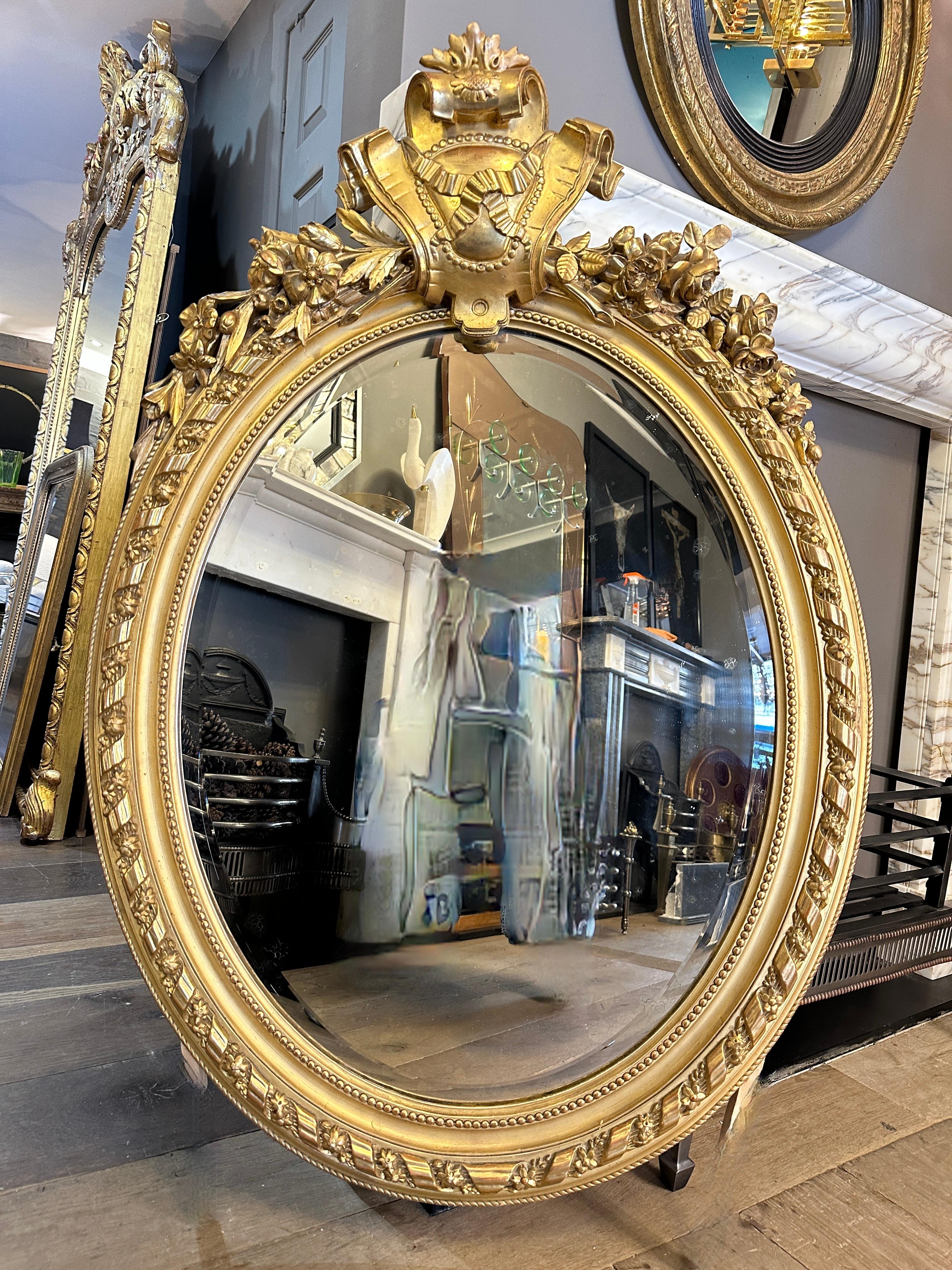 A large antique gold gilt Oval pediment mirror from the Napoleon III period. Very well decorated with inner beaded slip, ribbon twist floral edge and outer beaded frame. The central cartouche again of ribbon with a tied plain medallion, scrolled at
