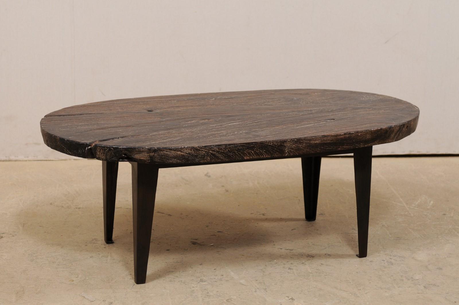 Table basse en bois de teck avec base en fer, créée sur mesure. Cette table basse à la fois rustique et chic a été fabriquée à partir d'une plaque de bois de teck de forme ovale, qui a été présentée sur quatre pieds en fer personnalisés. Le bois a